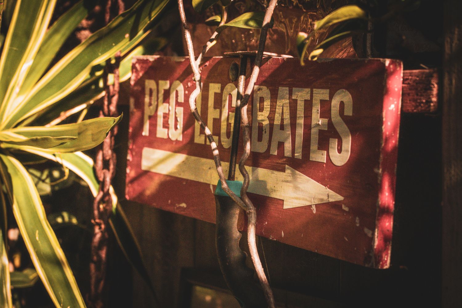 Vintage red metal 'Pirates Gates' sign illuminated among tropical plants.
