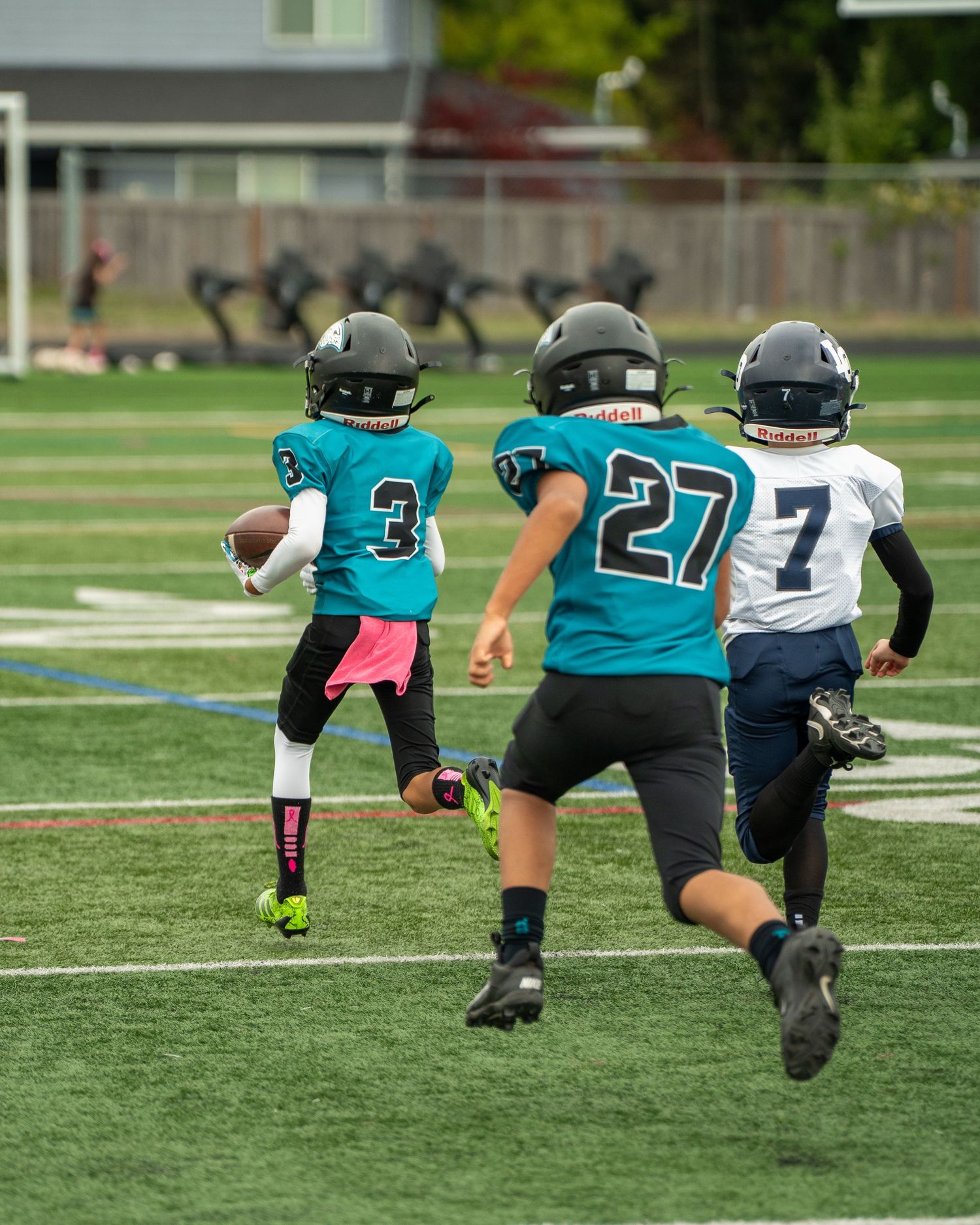 Football players in teal jerseys run plays during practice session.