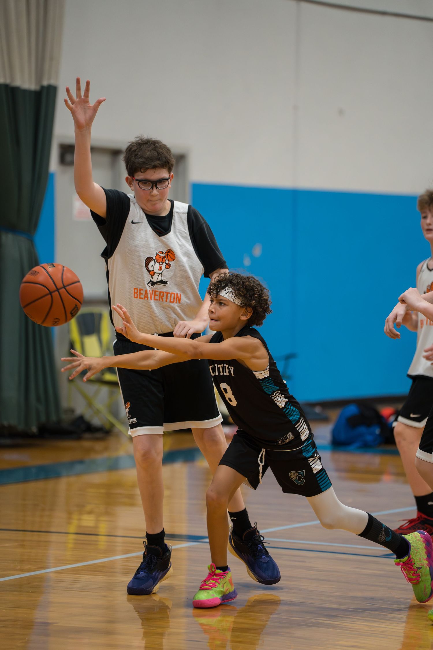 Basketball players dive for a loose ball during an intense youth game on a blue indoor court.