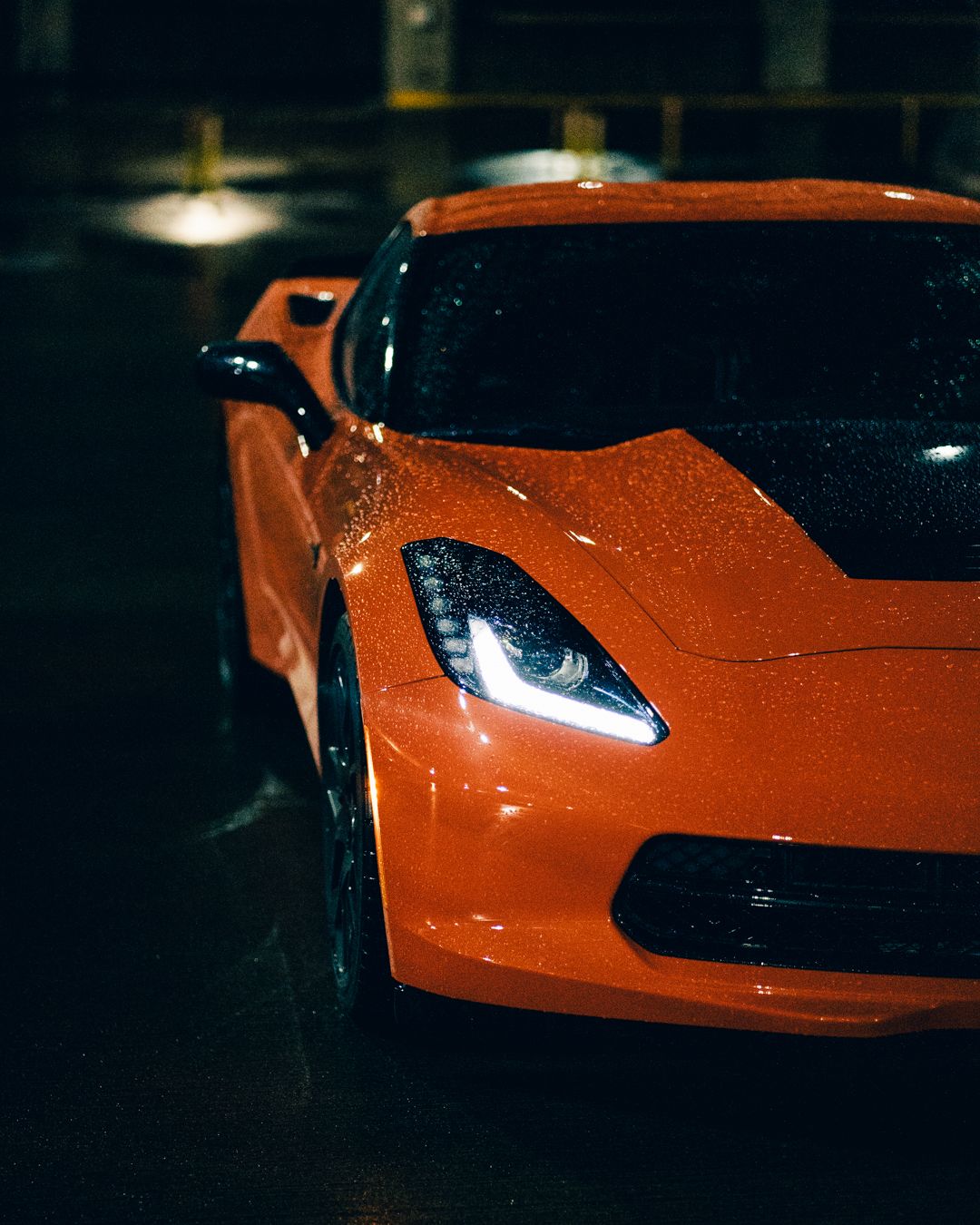 Orange sports car headlight detail shot in dramatic low-key lighting.