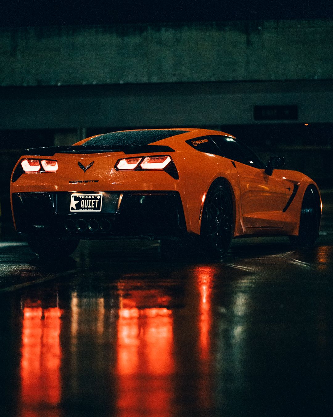 Wide shot of orange Corvette with red light reflections on wet floor.
