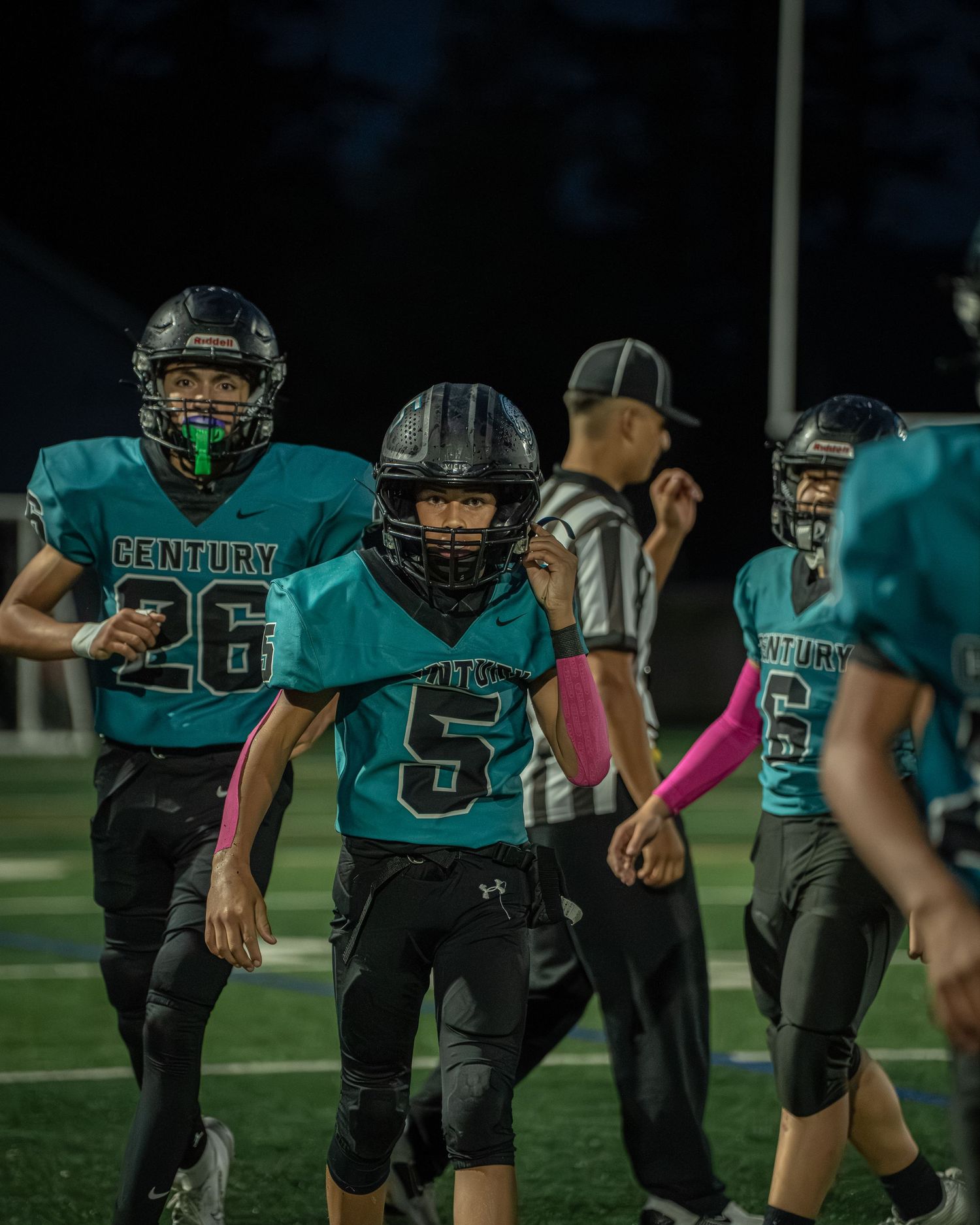 Football players in teal jerseys lined up in formation on a football field during practice.