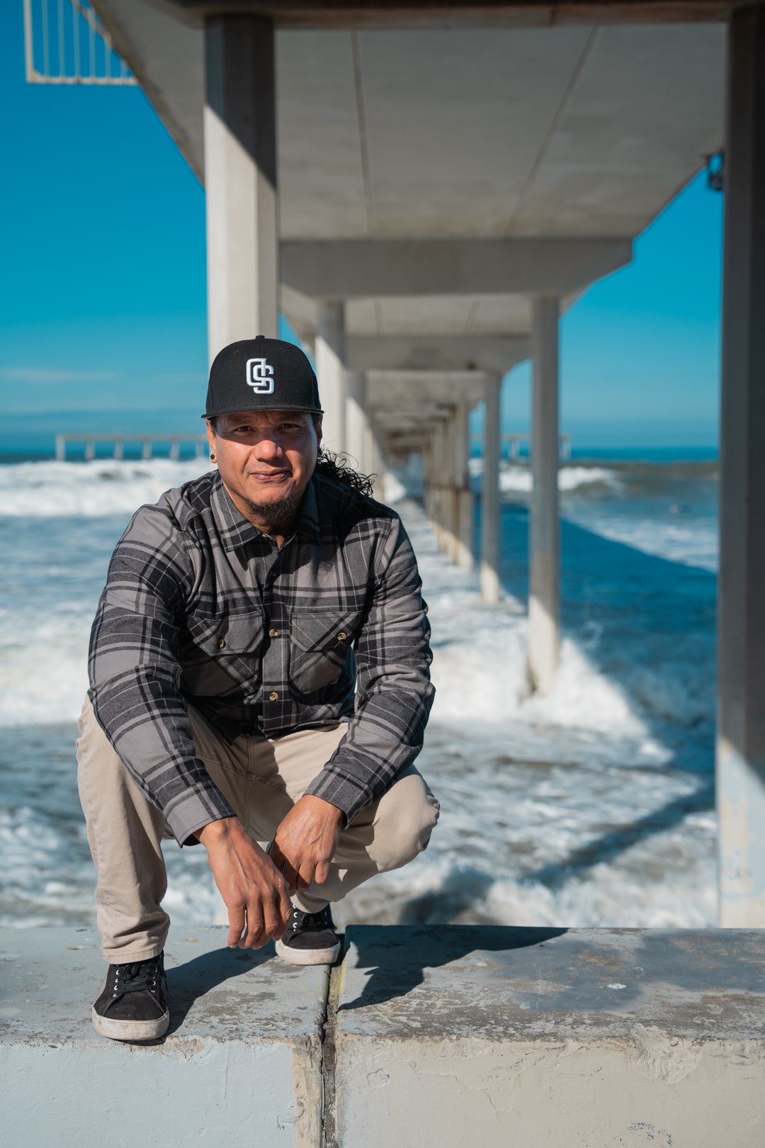 Person crouching on pier with crashing ocean waves in background.