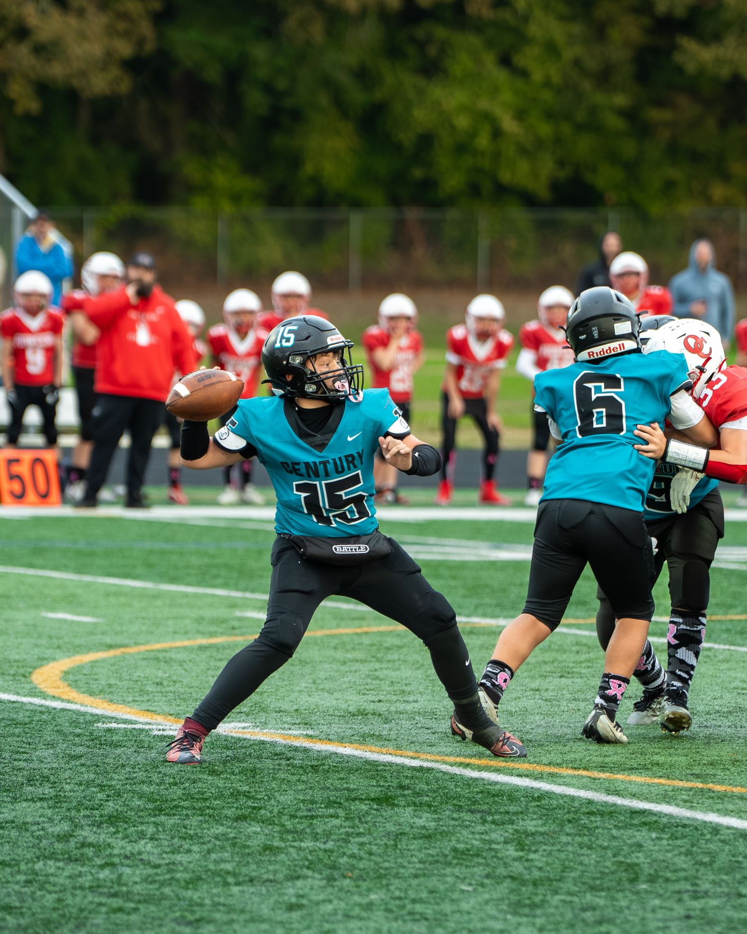 Football players in teal jerseys execute blocking formation during game play.