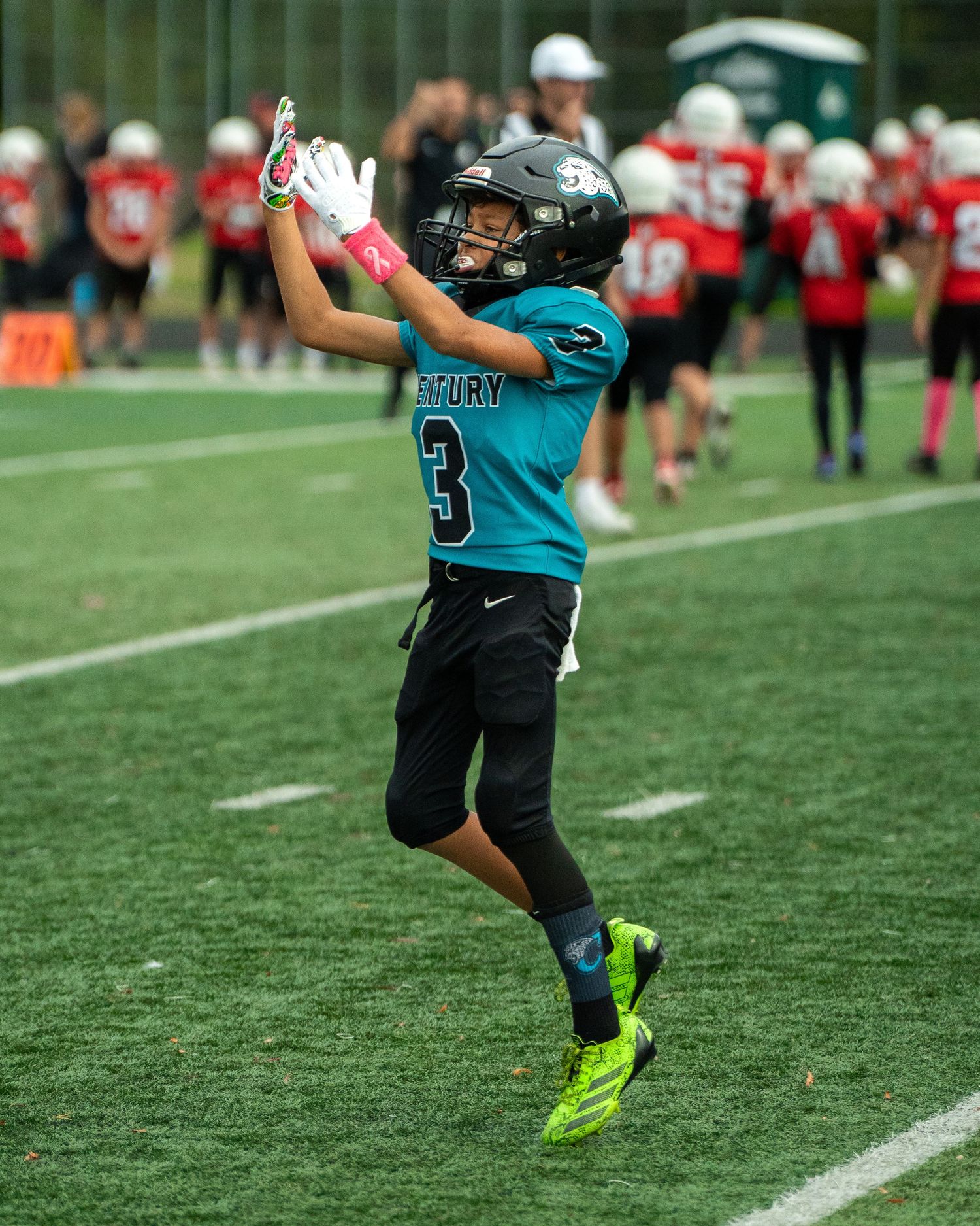 Young athlete in teal jersey number 3 practices kicking drills on football field.