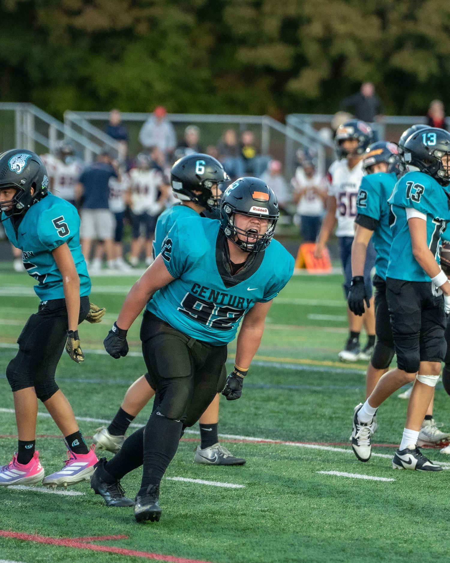 Football players in teal and black uniforms practice stance drills on the field.