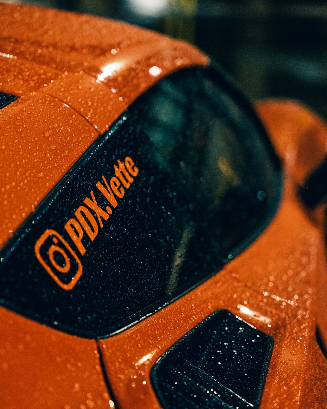 Raindrops on orange and black Genesis car hood creating textural detail.