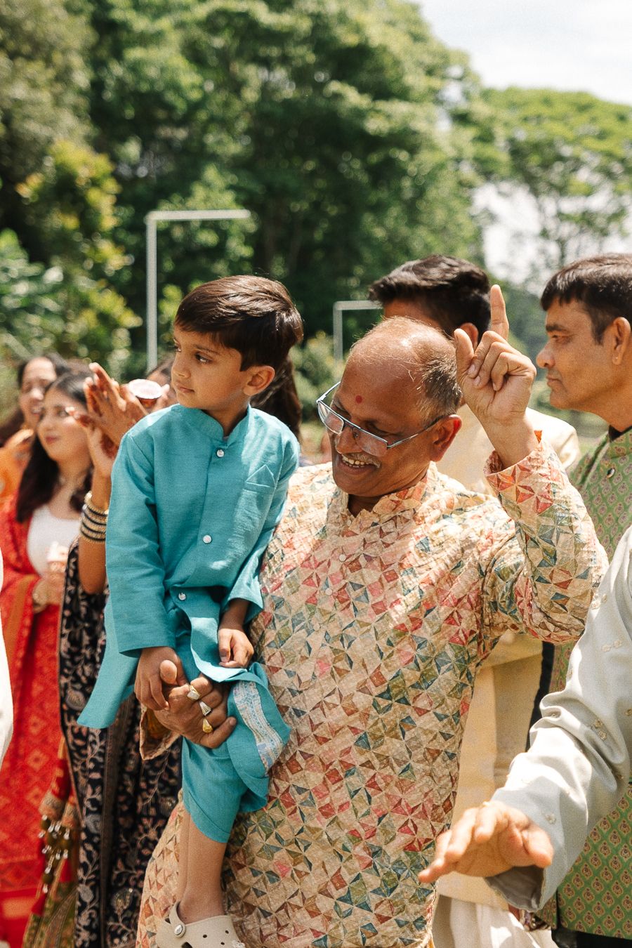 A group of people in traditional South Asian attire gather outdoors at a social event on a sunny day.