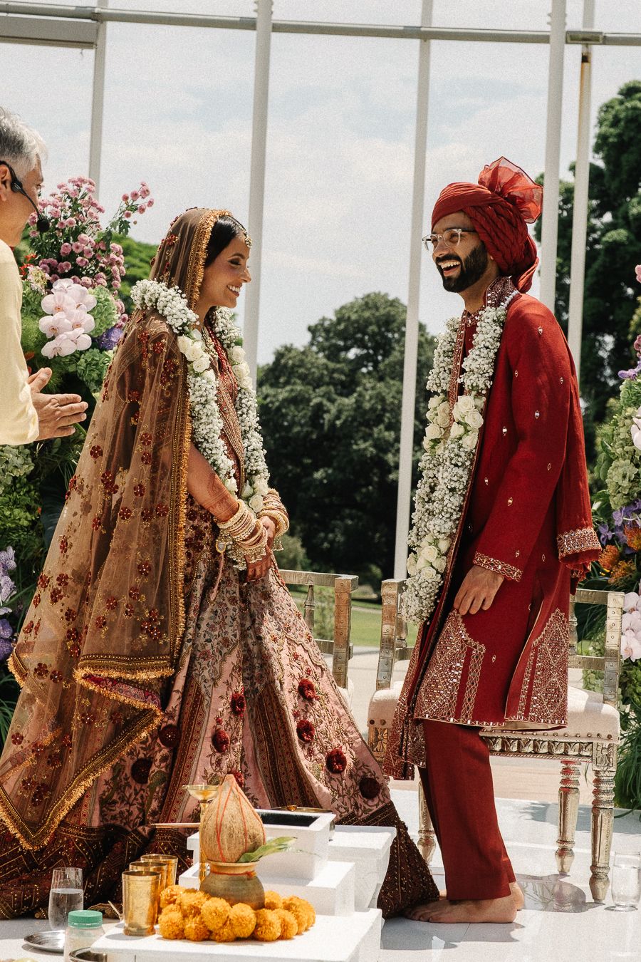 A traditional Indian wedding ceremony with a couple in ornate red and gold attire standing at a decorated outdoor venue.