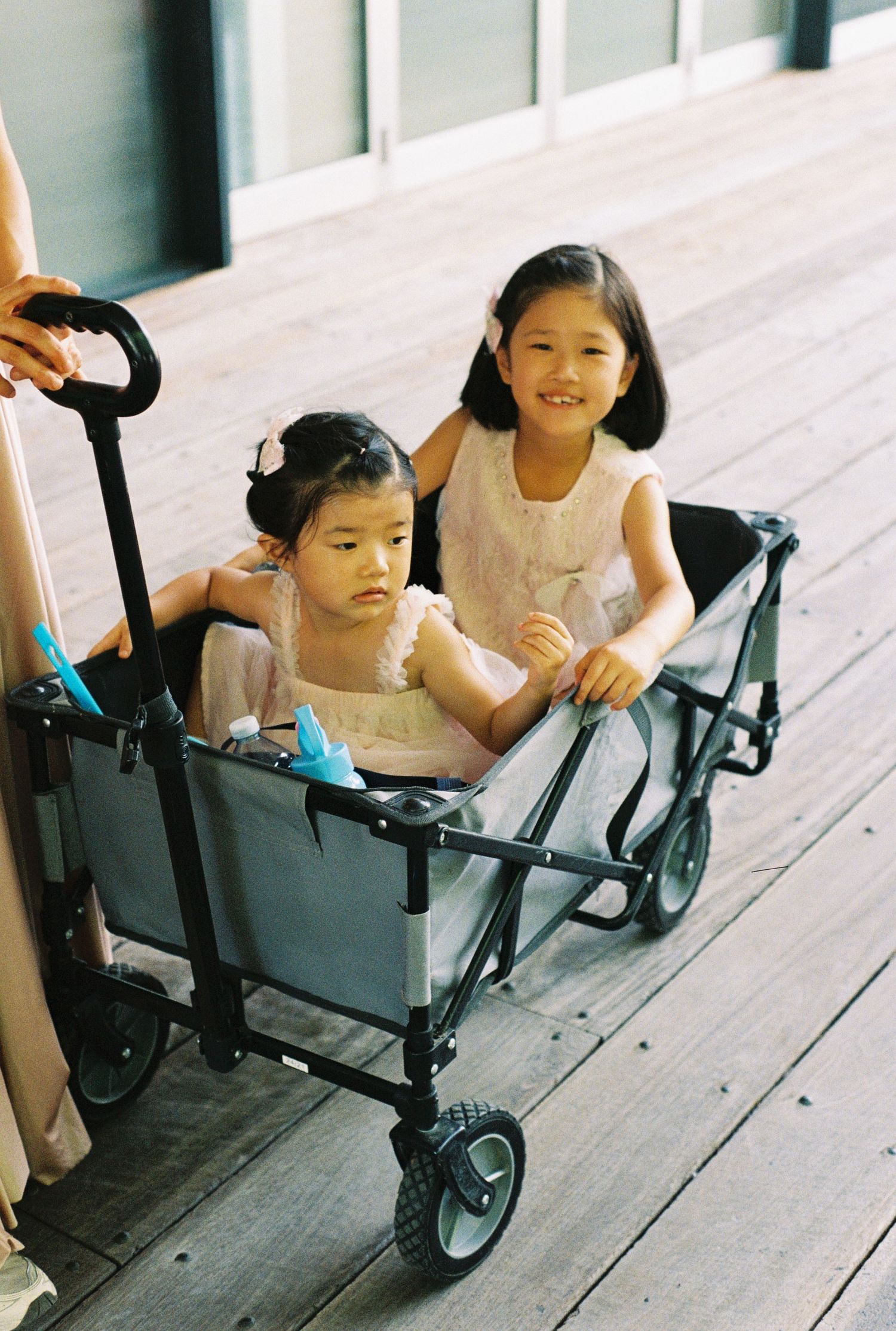 Children playing and crawling in a black utility wagon on a wooden deck in a playful sequence of photos.
