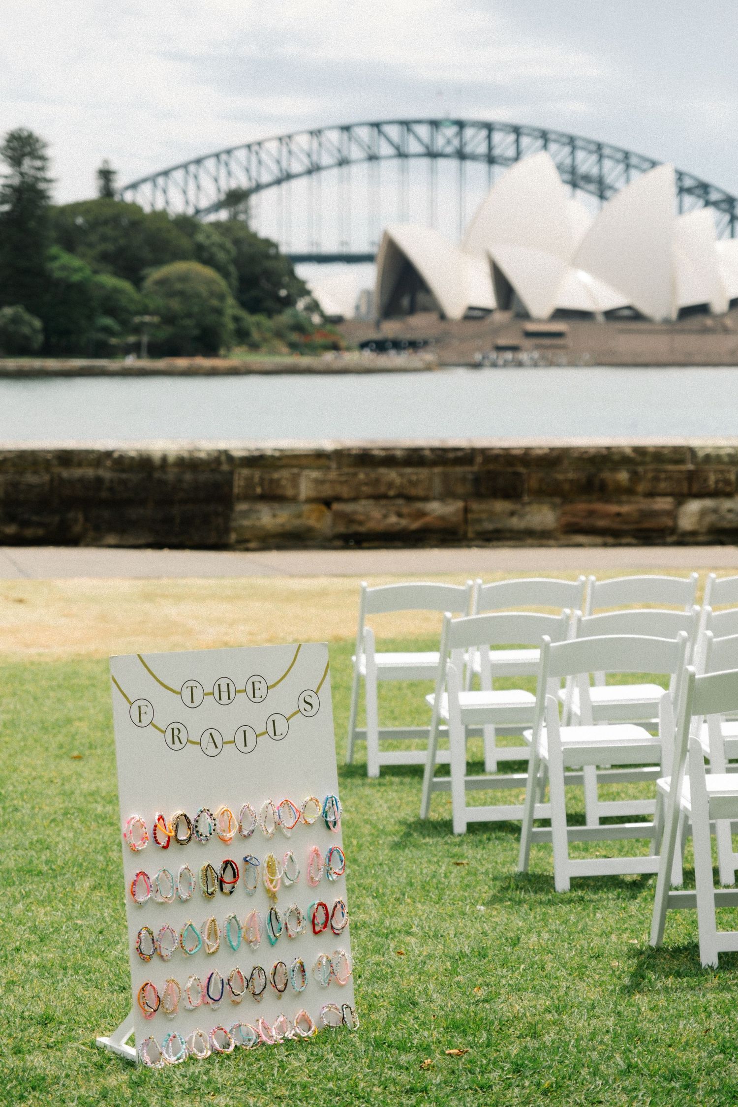 Outdoor wedding setup with white chairs and flip flop display stand overlooking Sydney Opera House and Harbour Bridge.