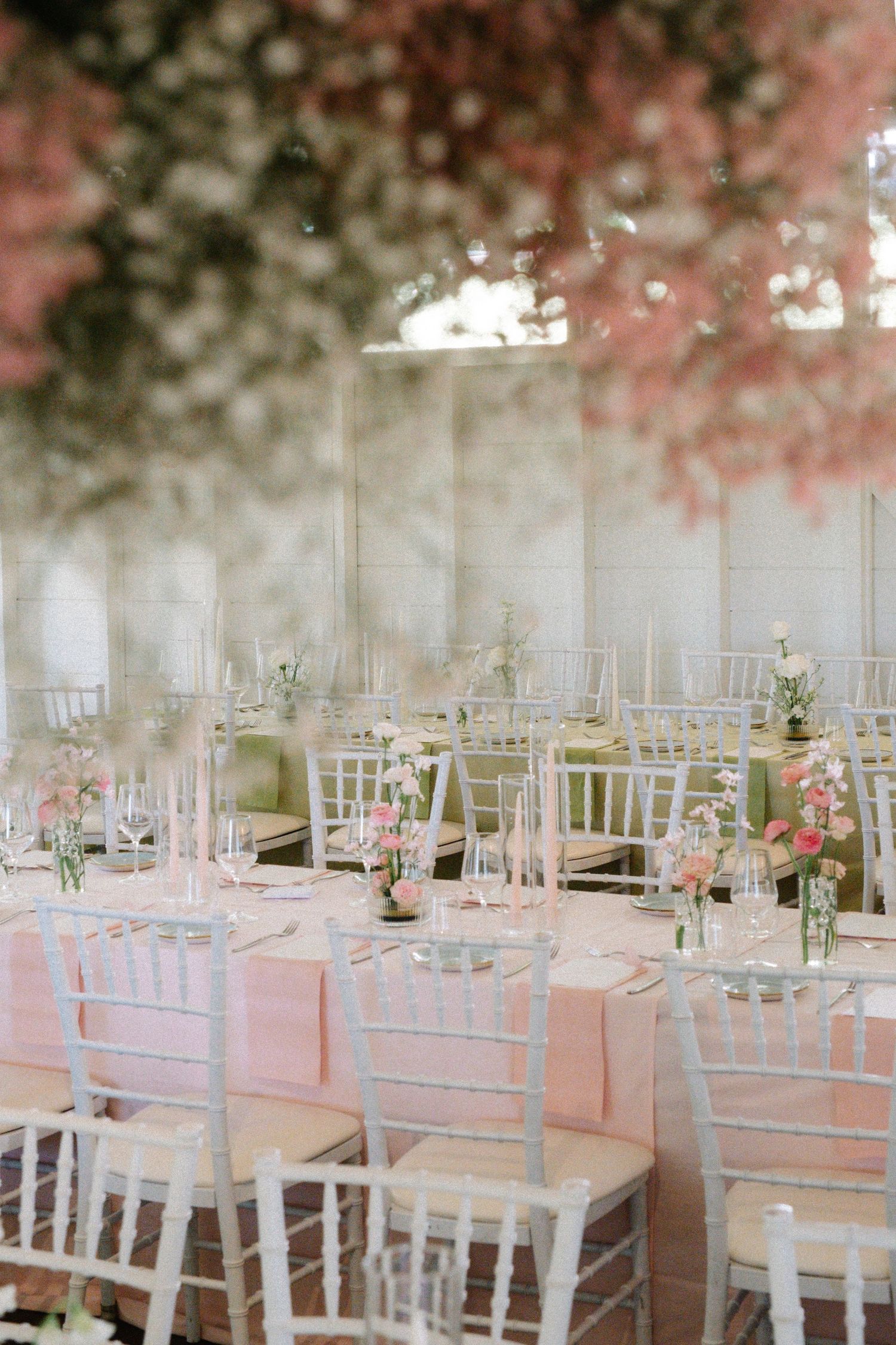 White chiavari chairs and pink linens create an elegant wedding reception setup under a dreamy tent canopy.