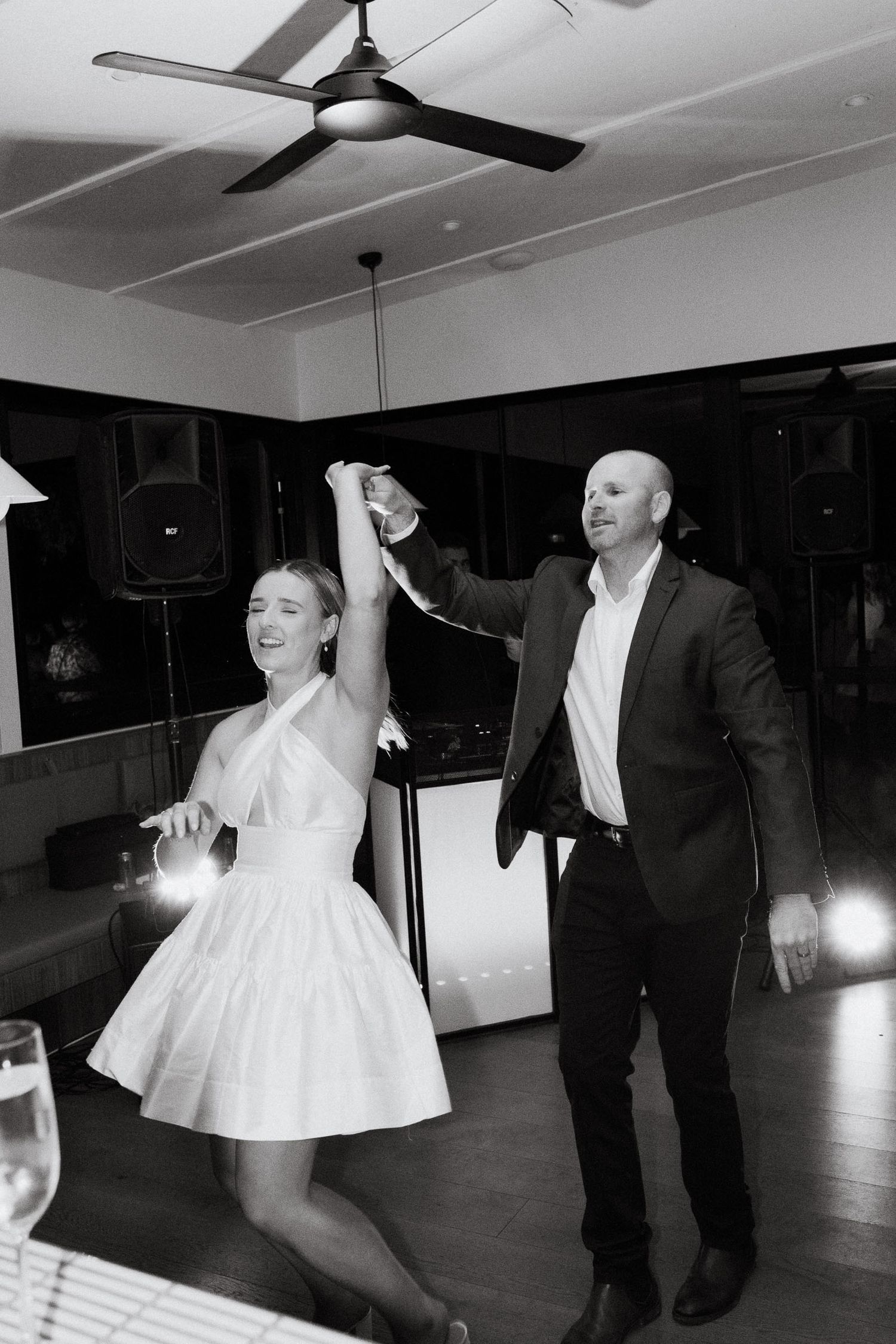 A couple dances together on a dark dance floor, with the woman wearing a white dress and the man in formal attire.