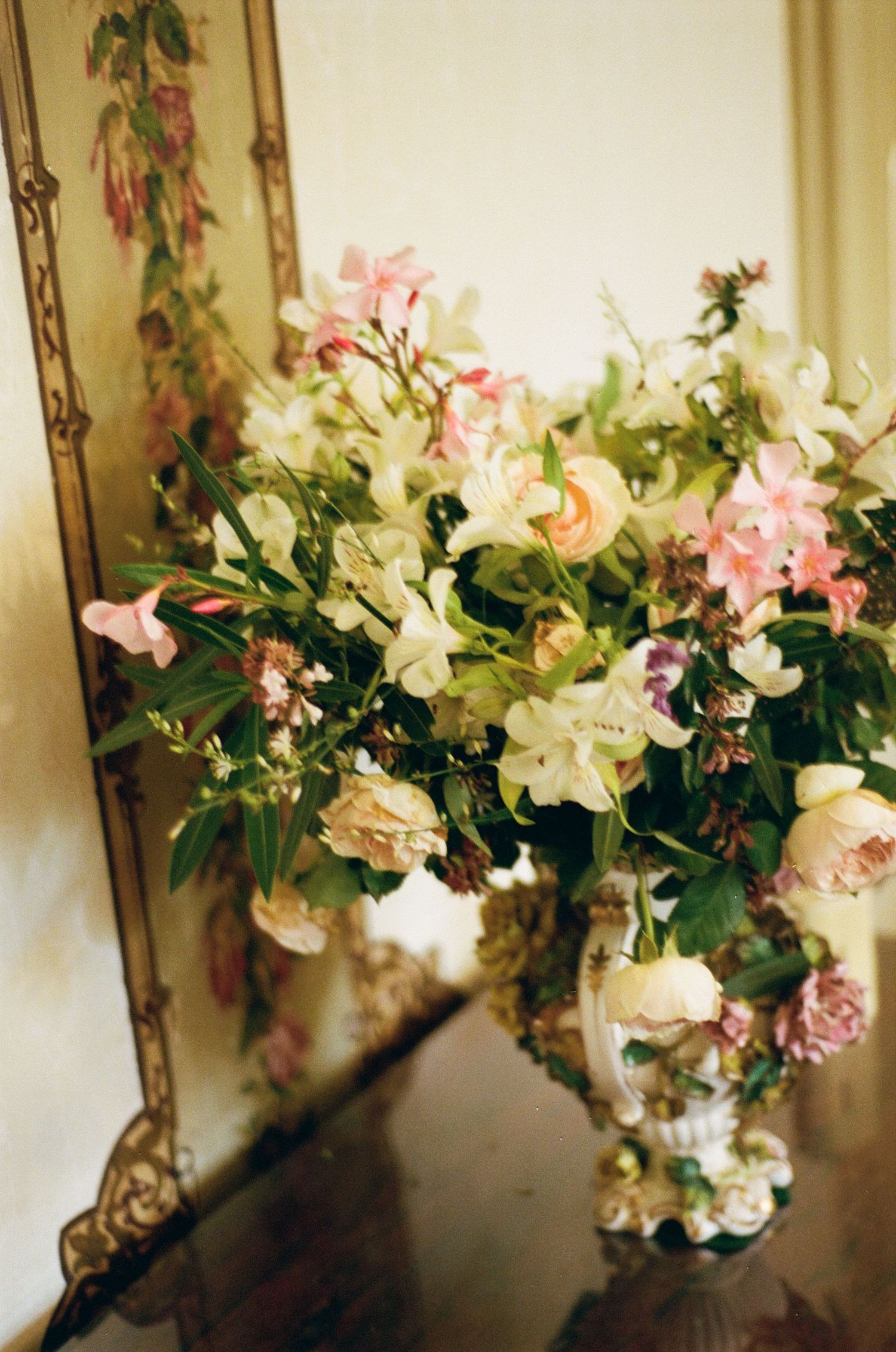 Delicate pink and white floral arrangement displayed against a warm-toned wall with ornate gold frames.