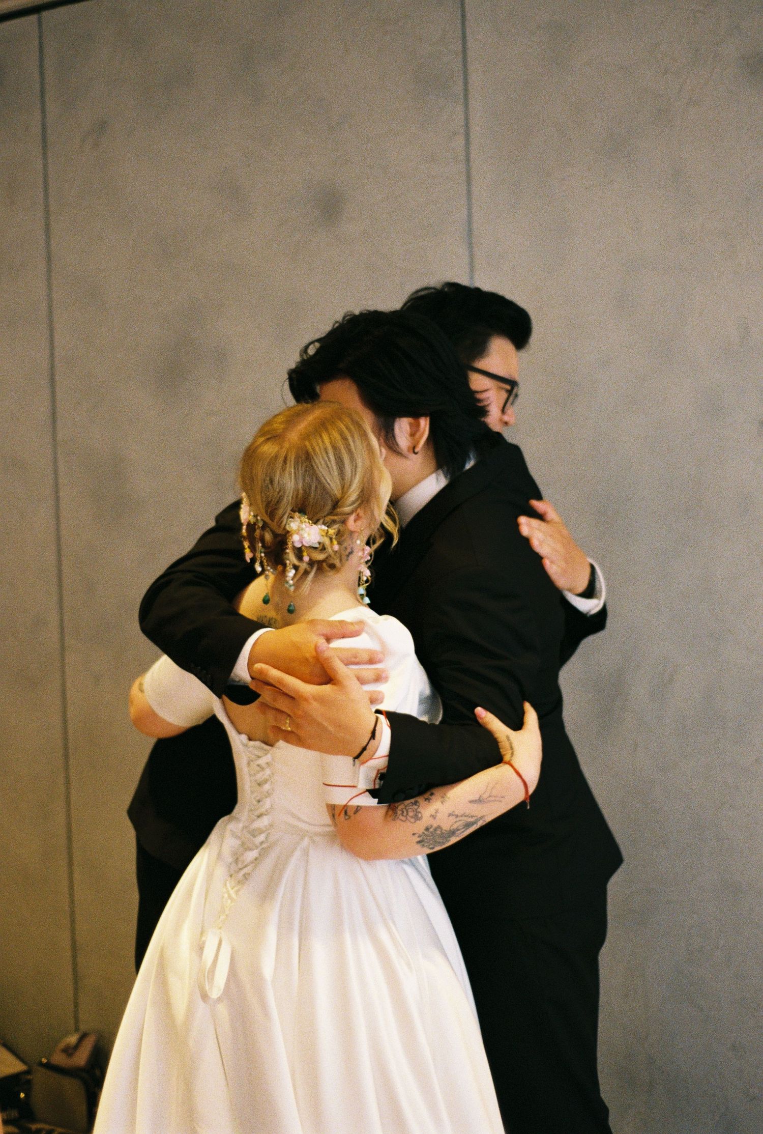 A couple in formal attire dancing together in an elegant ballroom setting against a neutral backdrop.