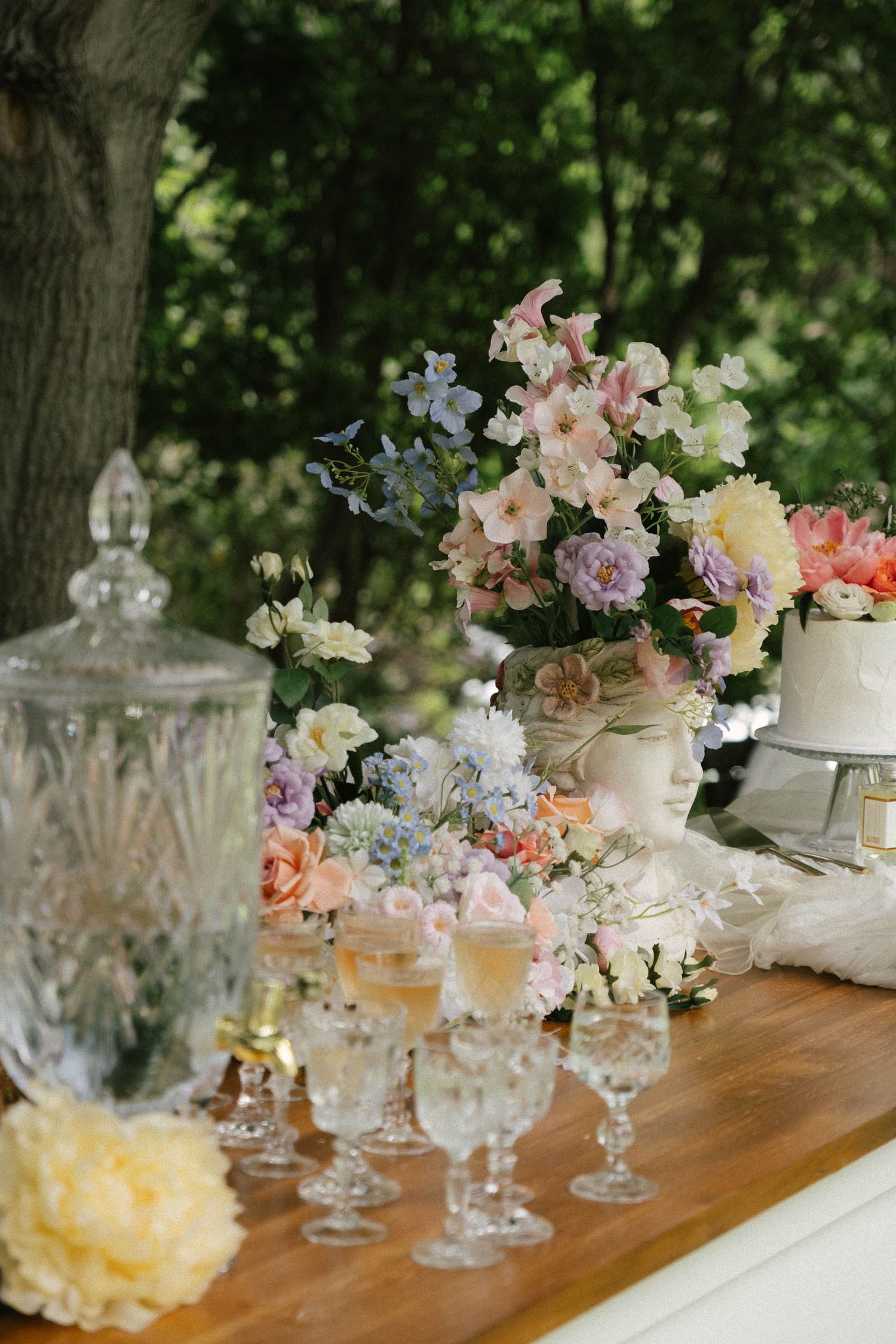 Elegant table setting with crystal glassware and pastel floral arrangements in white vases on a wooden surface.