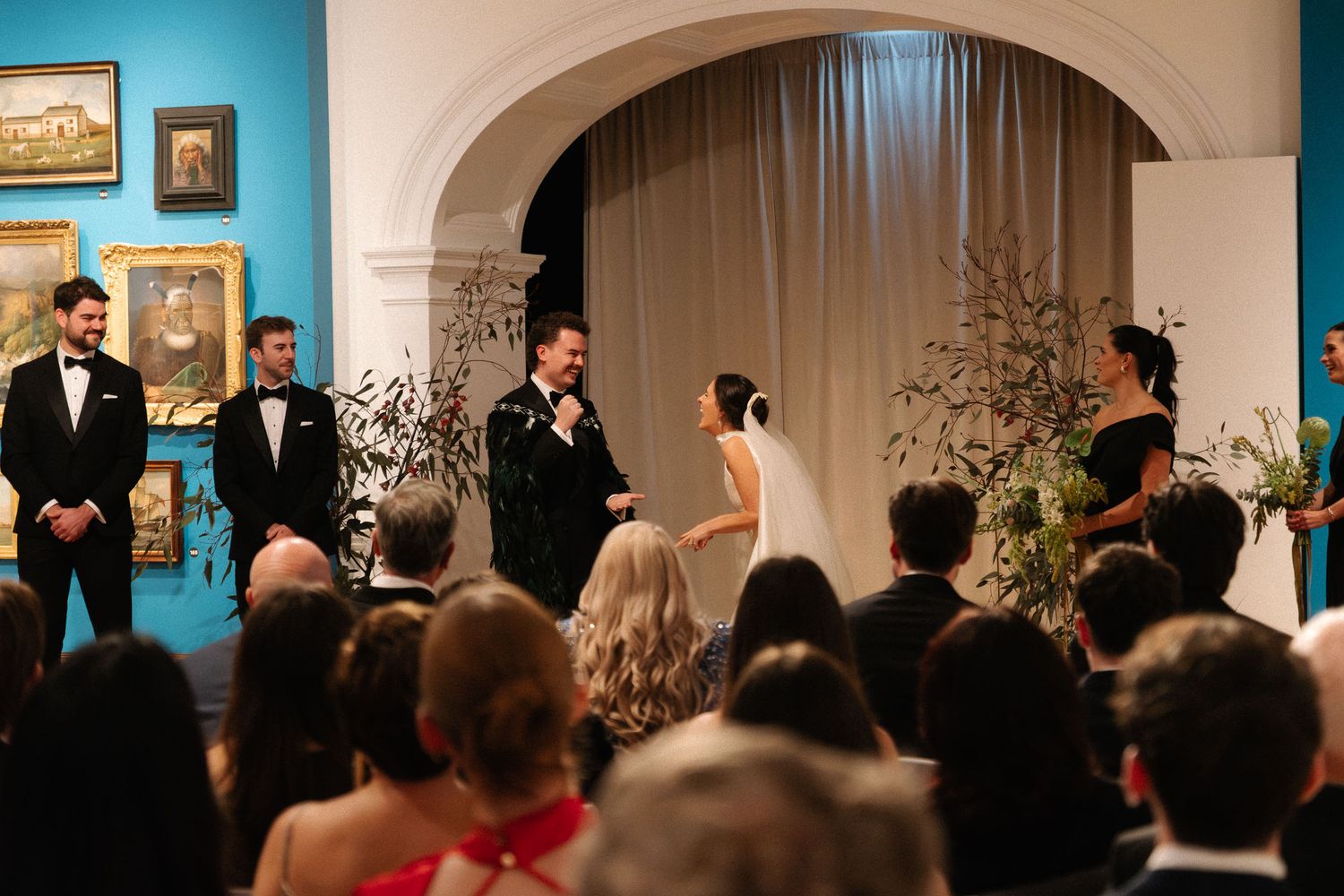 A formal wedding ceremony takes place under an elegant archway with guests seated in rows watching the proceedings.