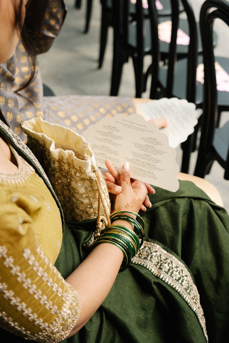 Person wearing traditional embroidered green and gold dress with intricate lace details and bangles on their wrist.