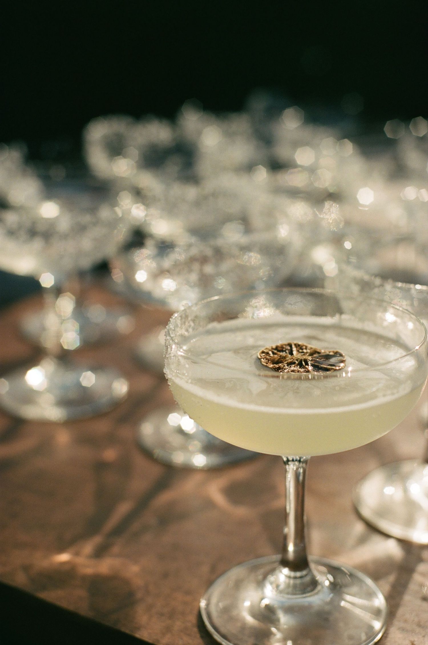 A classic coupe glass filled with frothy cocktail garnished with a delicate flower on a dark wooden surface.