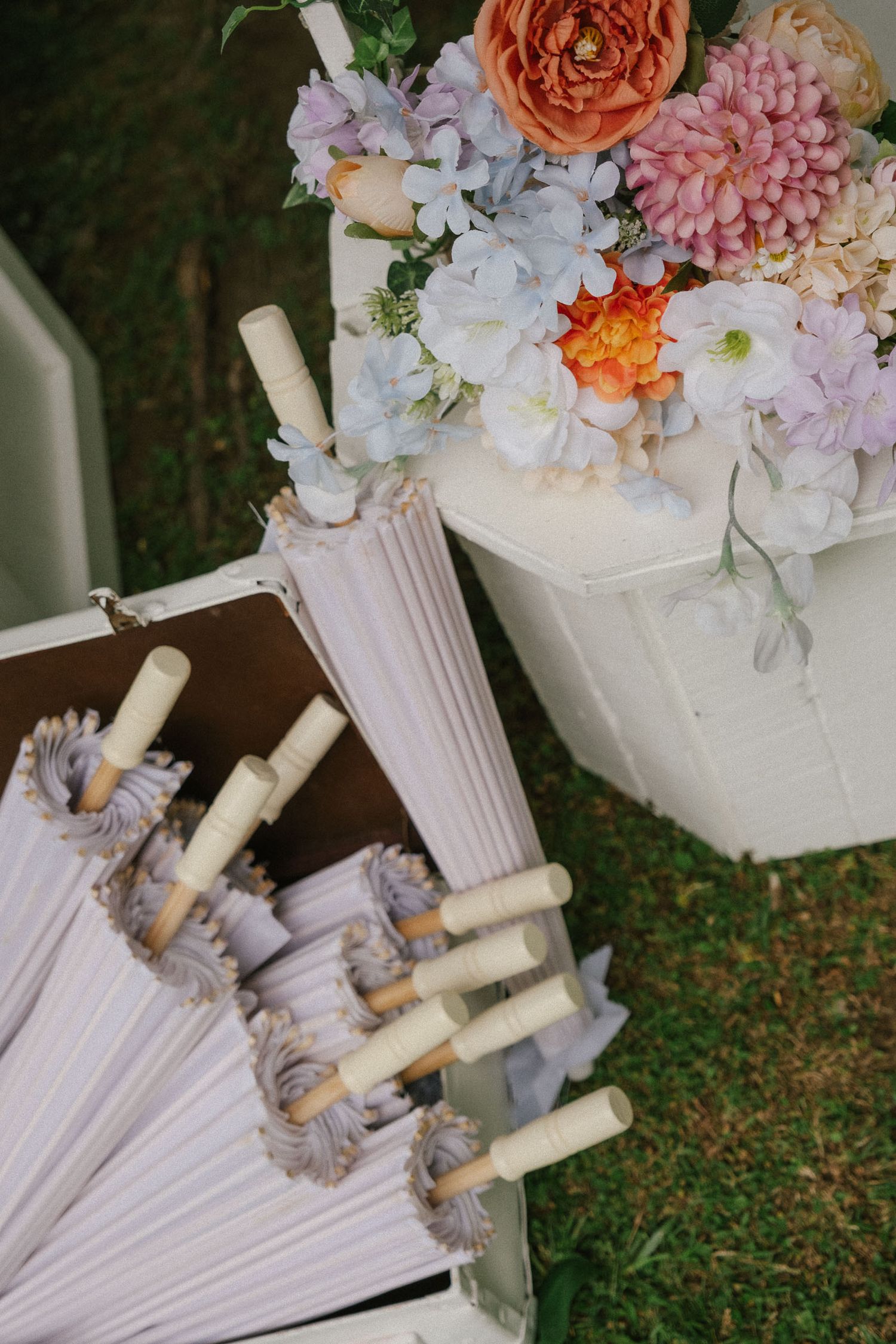 White parasol with floral decorations in coral and pink lies on grass with delicate scattered petals.
