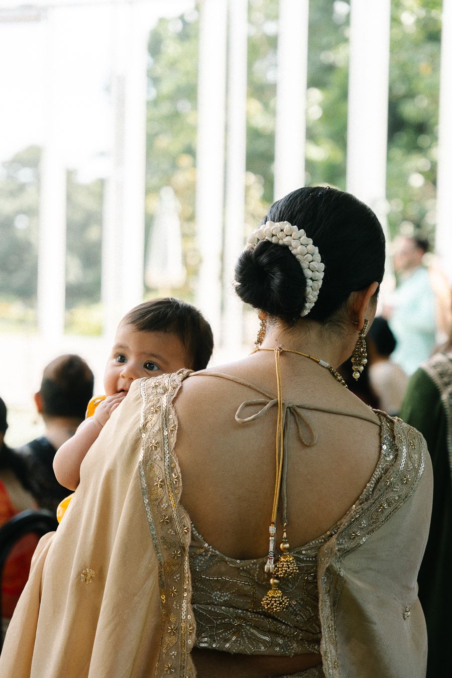 A row of wedding guests in formal attire with embellished necklines and lace details viewed from behind.