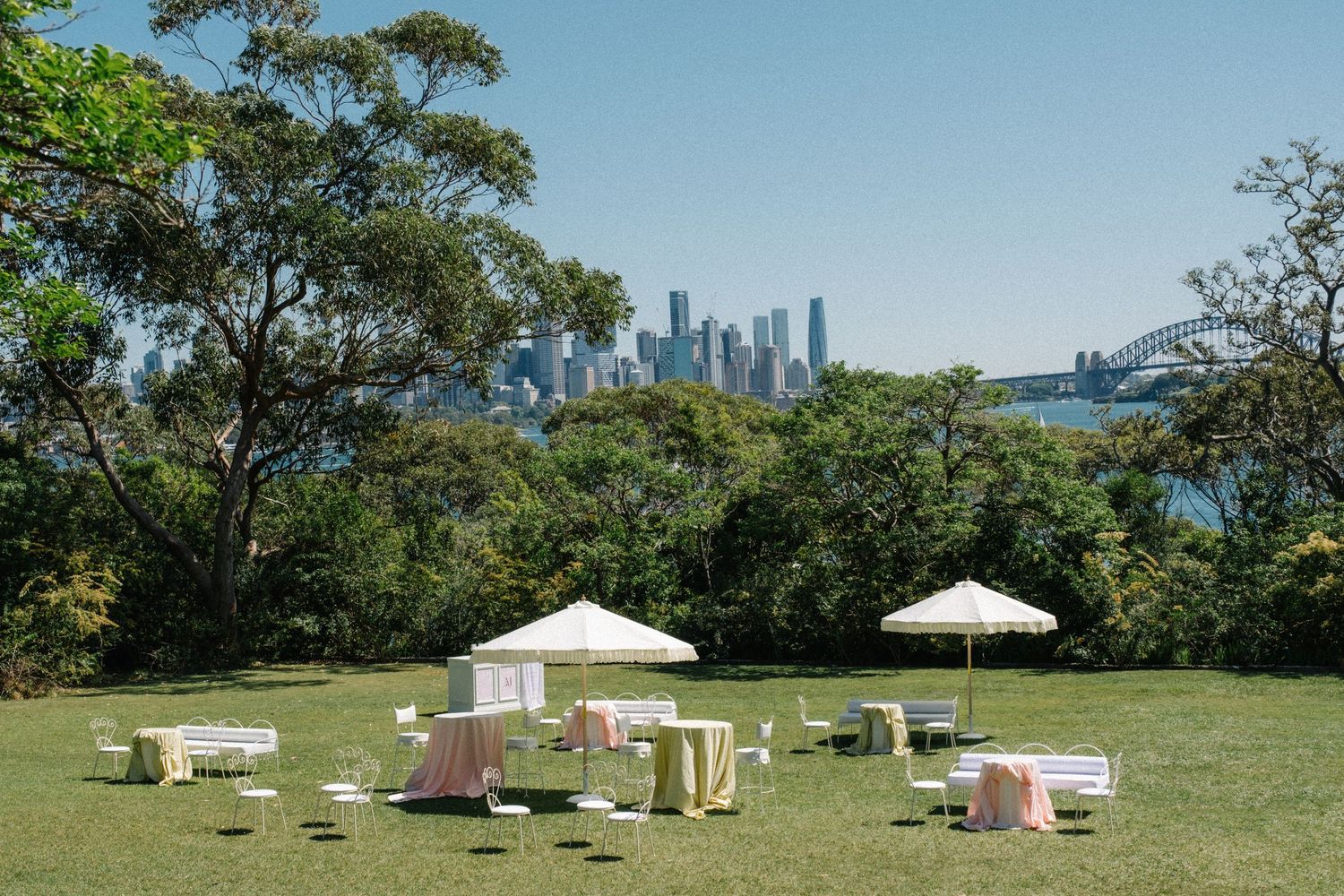 White yurts and tents dot a grassy hilltop with distant city skyline views on a sunny summer day.