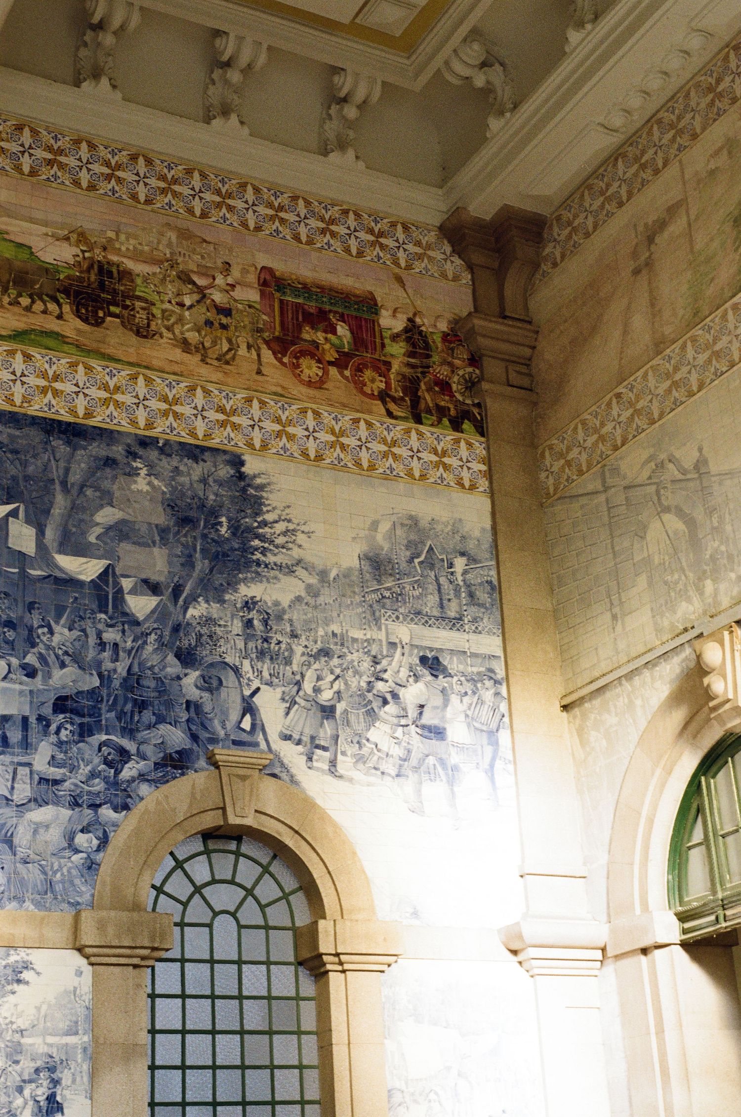 Blue and white azulejo tile murals depicting historic scenes line the walls of a grand station hall with arched windows and ornate cornices.