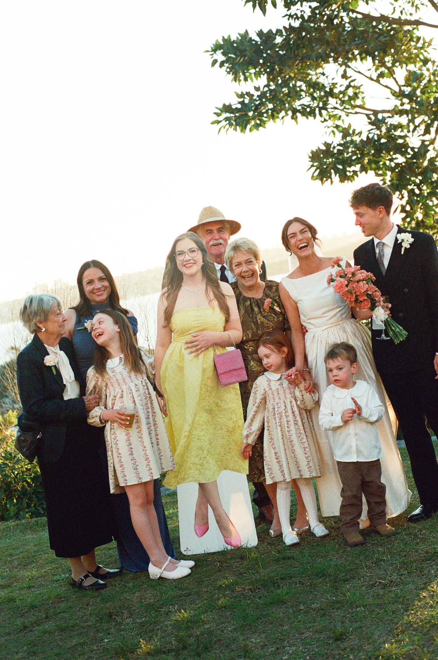 Wedding family portrait with bride holding coral bouquet and groom in white boutonniere outdoors.