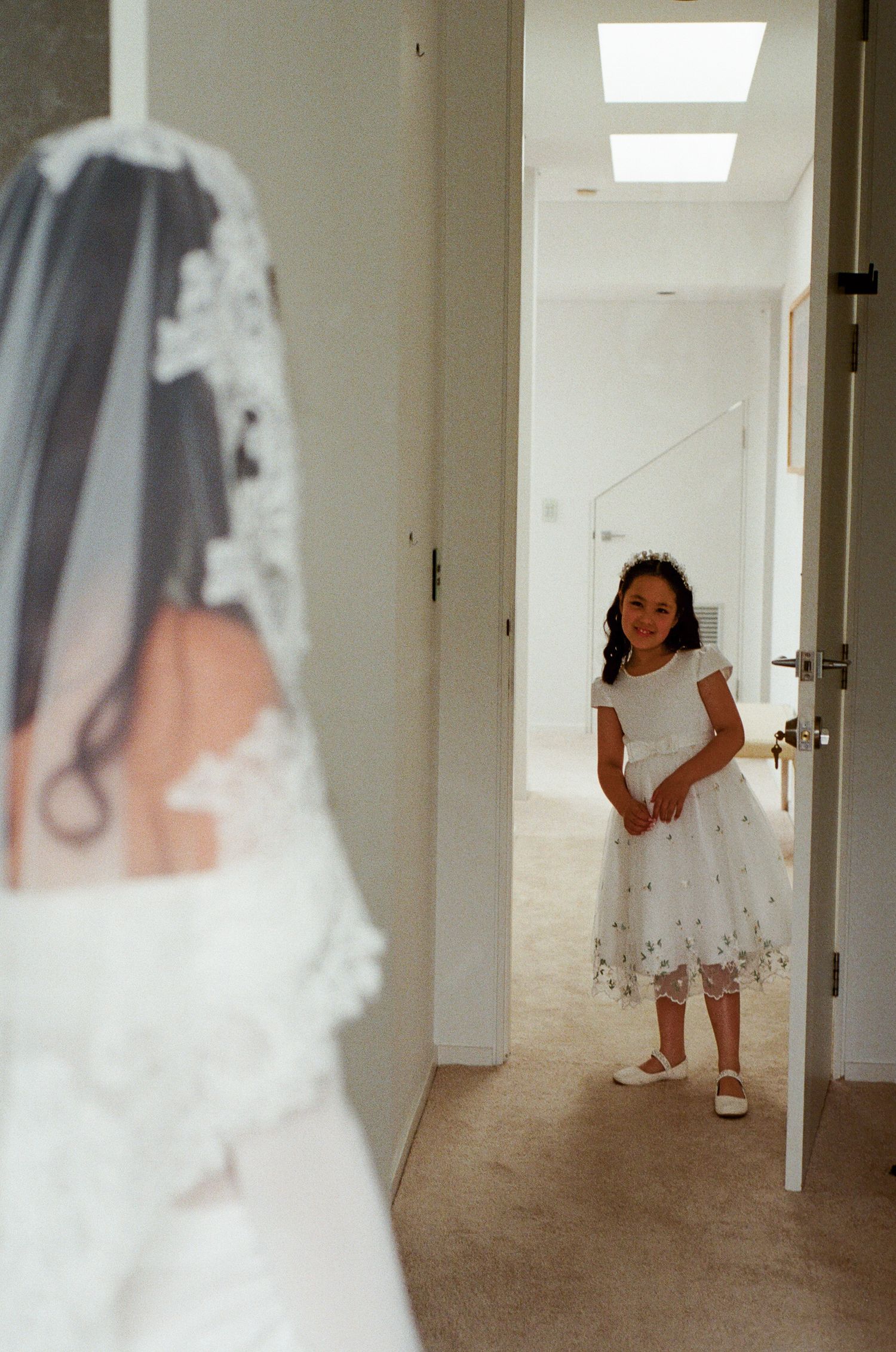 A person in a white dress stands in a bright hallway with multiple doorways and natural light streaming in.