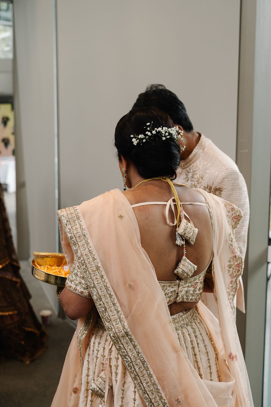 Bridesmaids wearing matching peach-colored sarees with delicate lace details stand in a row at an elegant wedding.