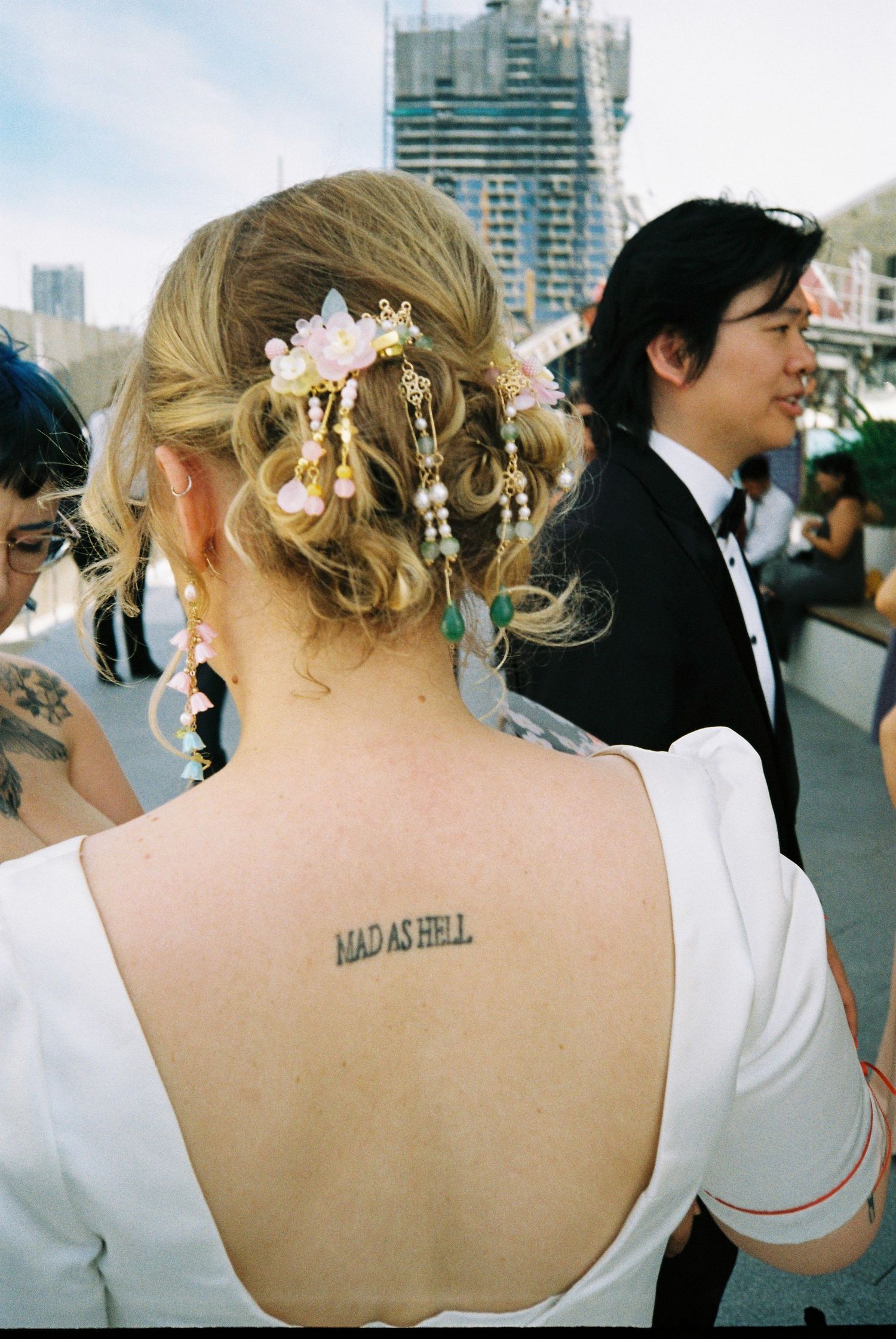 A series of photos showing a tattoo reading 'MAD AS HELL' on someone's upper back at what appears to be a formal event.