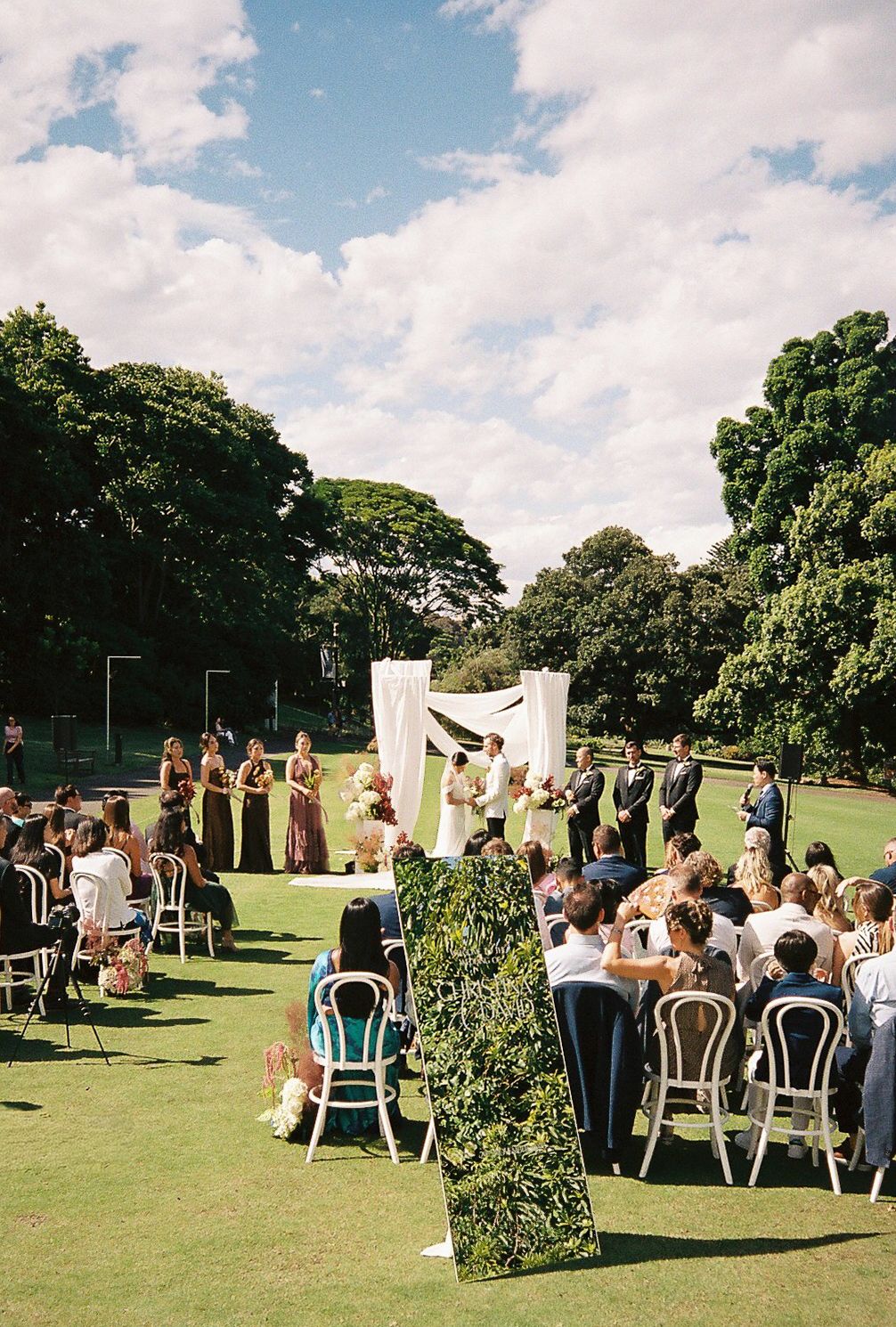 An outdoor wedding ceremony setup on a grassy lawn with white chairs and decorative elements under a blue summer sky.