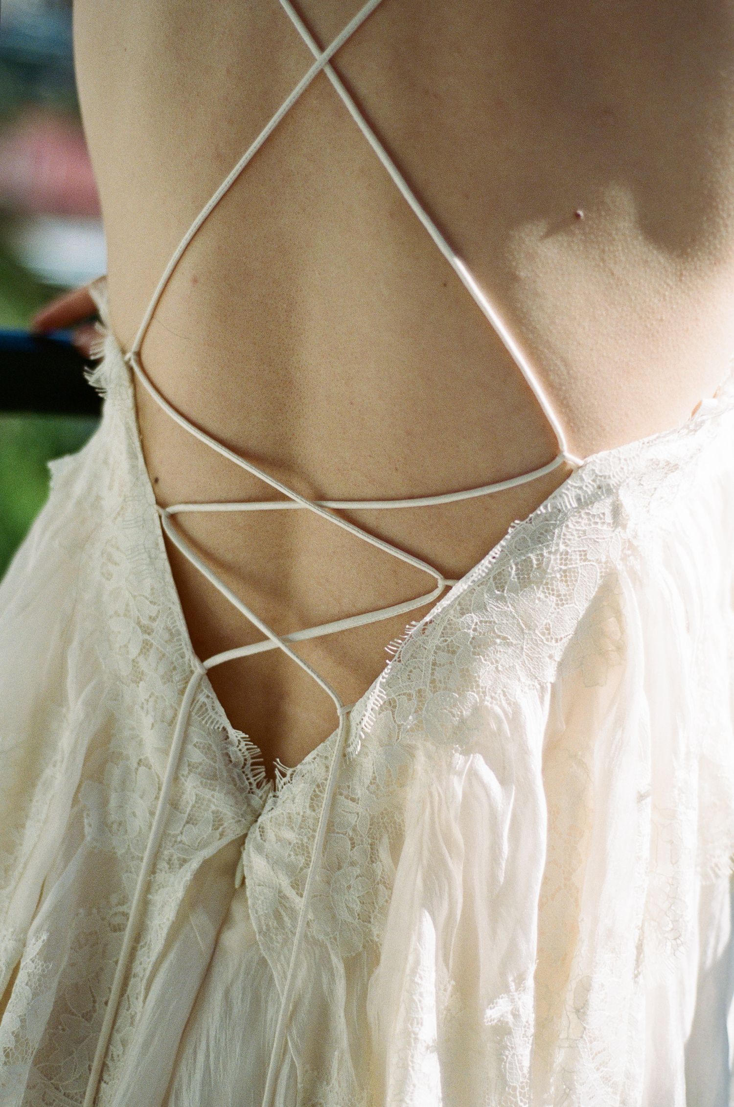 Back of an ivory lace wedding dress with delicate criss-cross lace-up straps and flowing, feathery fabric in soft natural light.