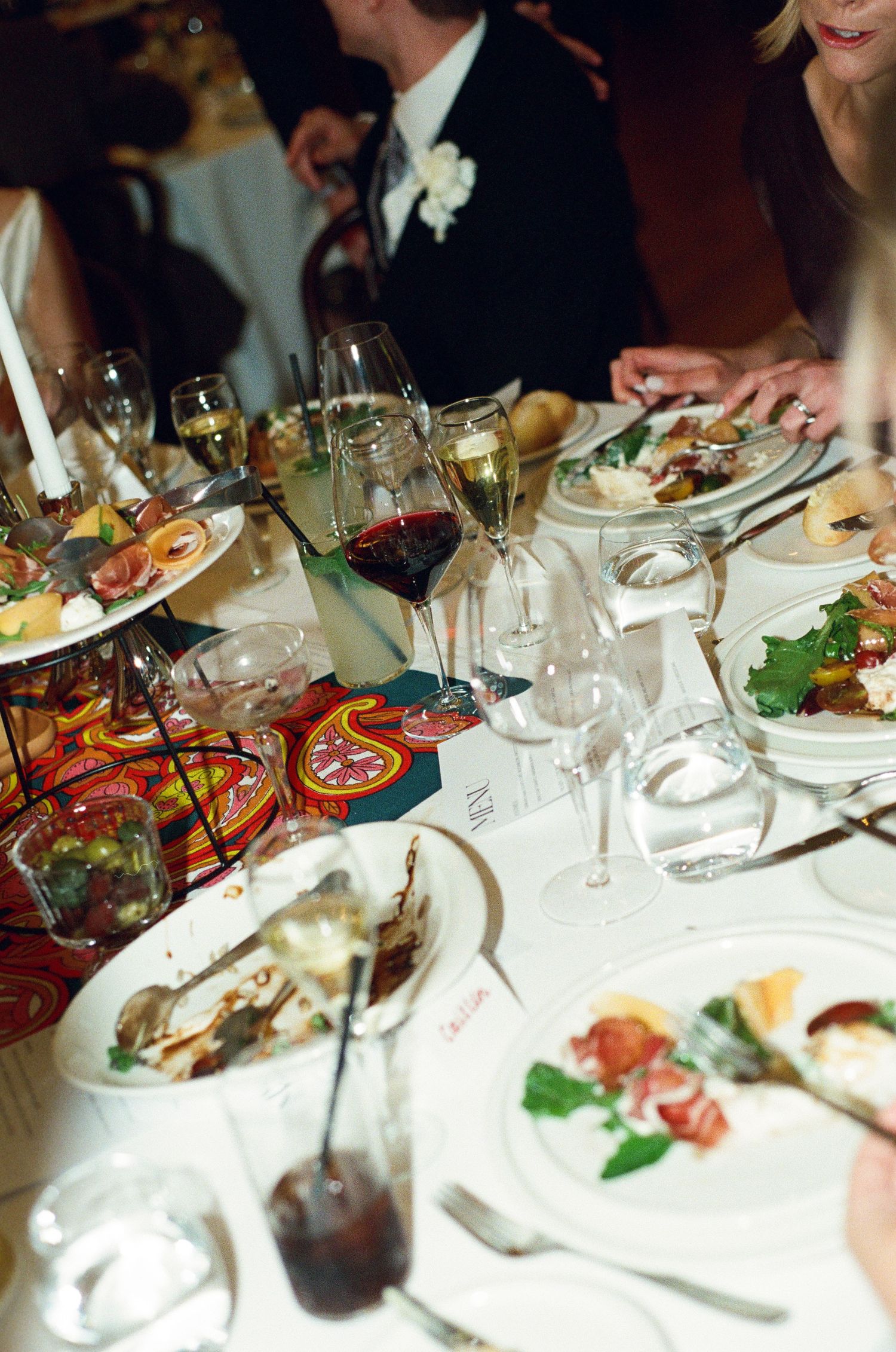 Elegant wedding reception dinner table with wine glasses, gourmet food, and candlelight decor.