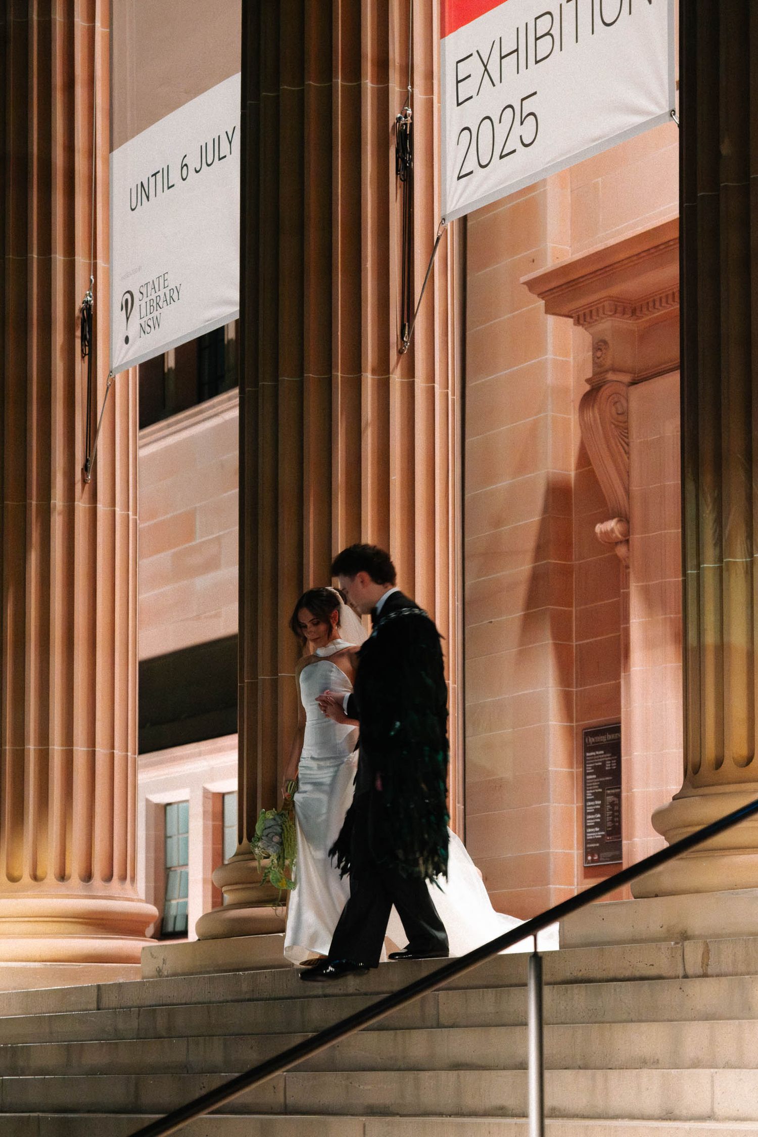 A couple in formal wear descends stone steps outside a columned building at night.