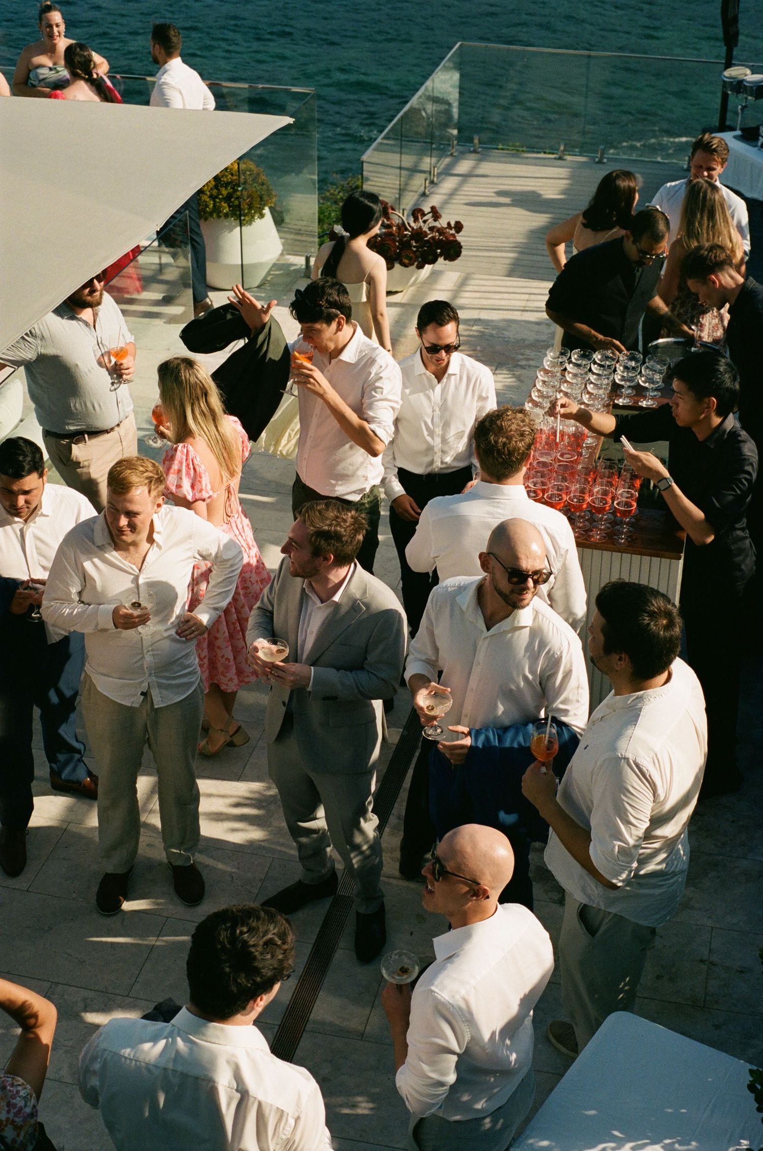 A group of people gathered at an outdoor party near the water, dressed in white and casual attire.