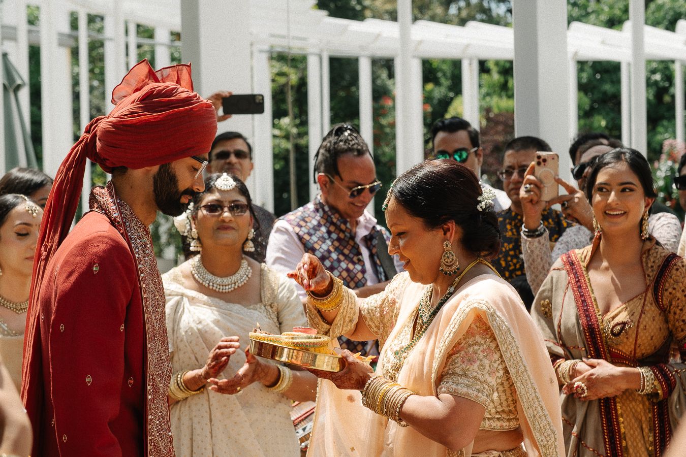 A large group of people in traditional Indian wedding attire gathered for a celebration with bright red and gold colors.