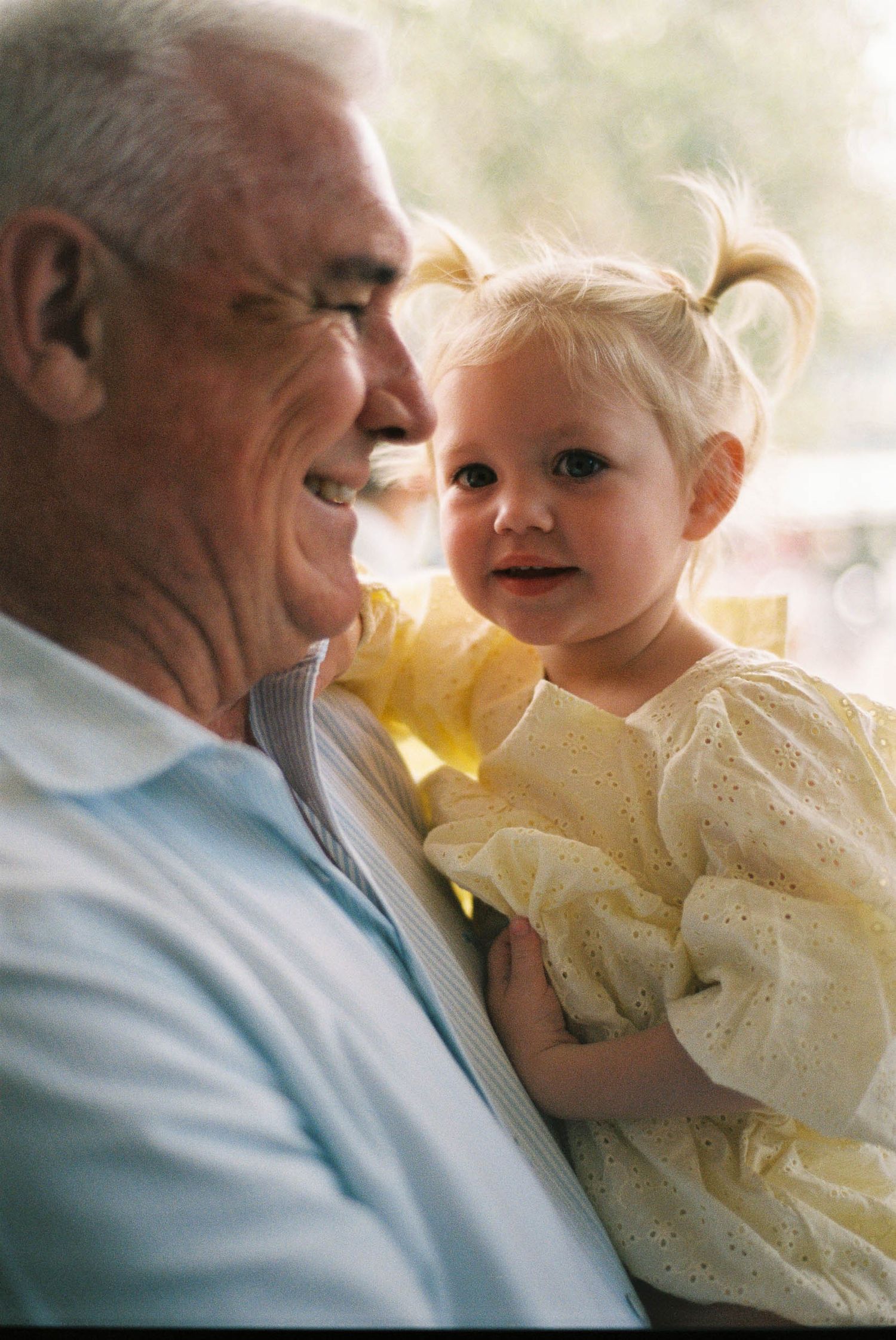 A heartwarming moment shows a senior in a light blue sweater sharing a joyful laugh with a small child in a yellow dress.