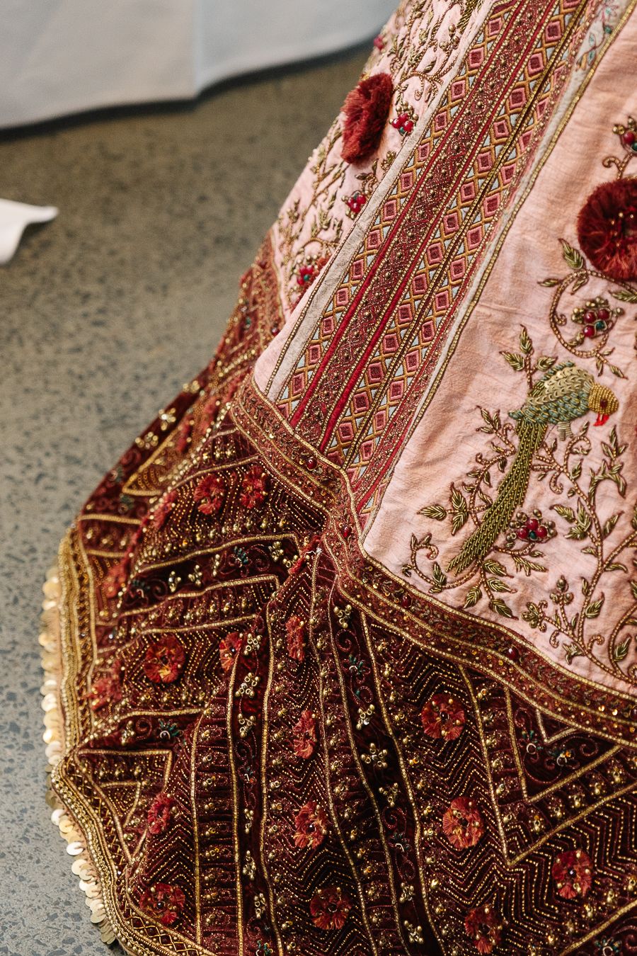 Close-up detail of ornate beadwork and embroidery on a pink and burgundy traditional Indian wedding garment.