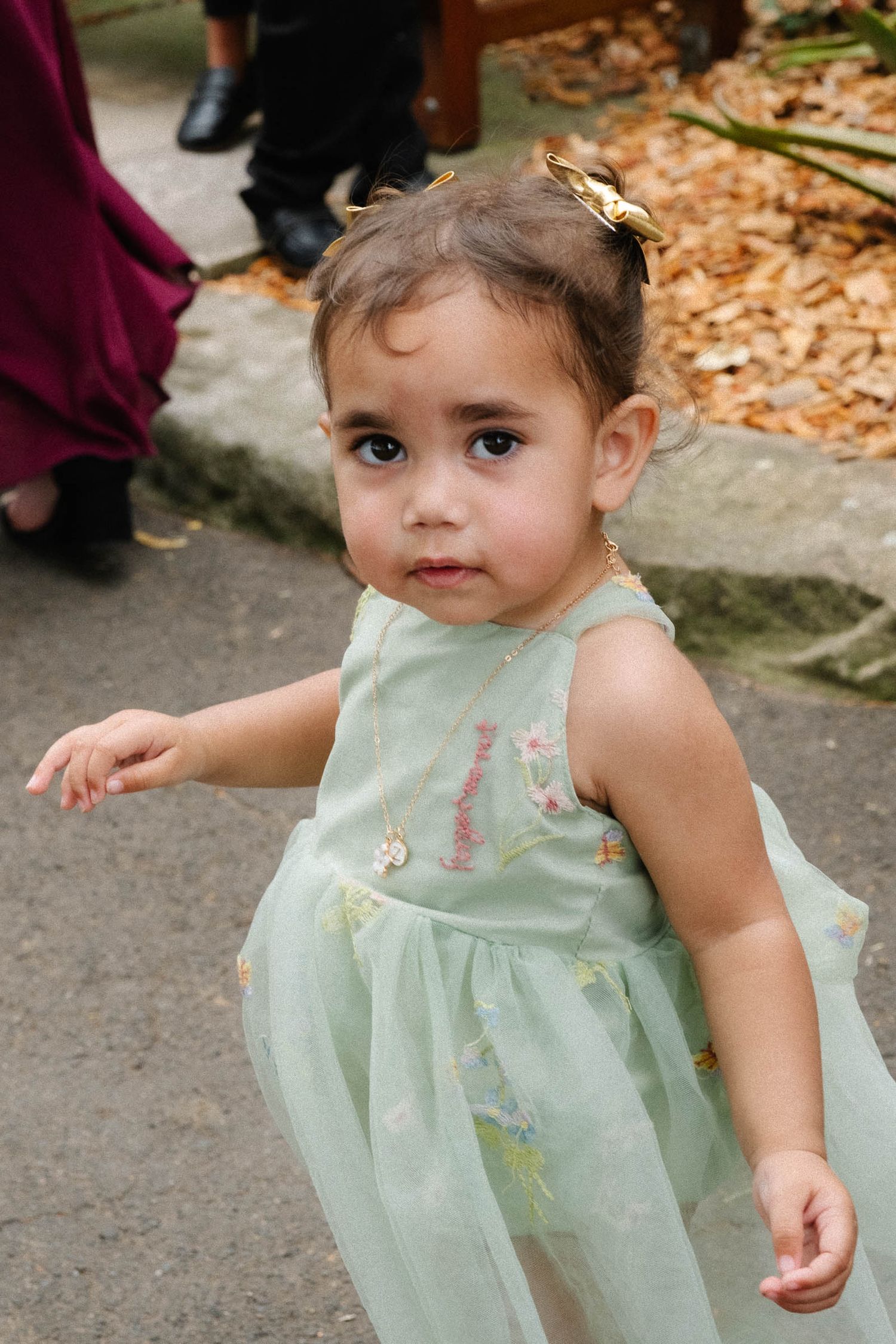 A toddler in a mint green dress plays outdoors among fallen autumn leaves.