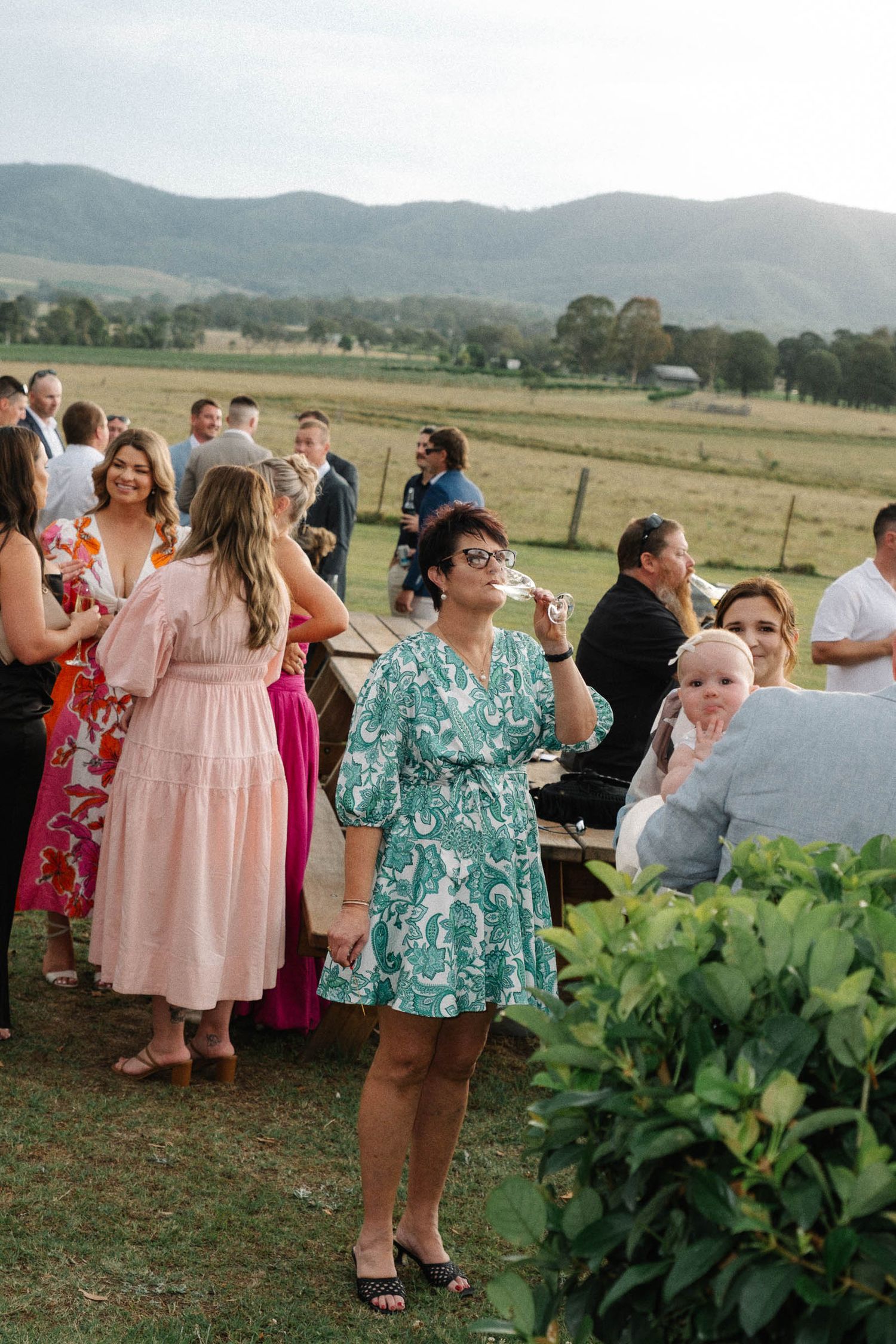 Wedding guests mingle and socialize at an outdoor reception with mountain views in the background.