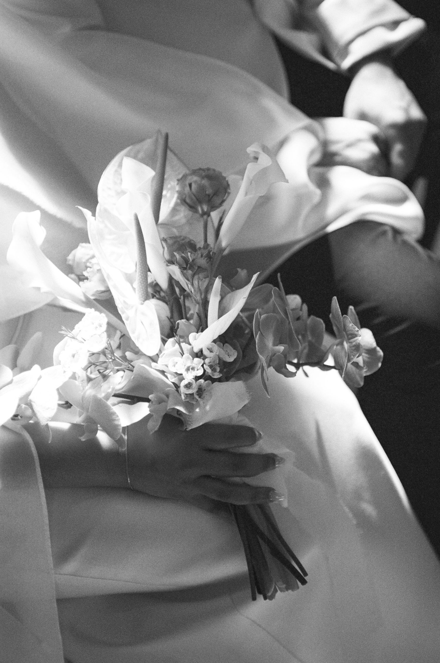 Black and white photo of a bride in a white gown holding an elegant bridal bouquet of lilies and small blossoms.