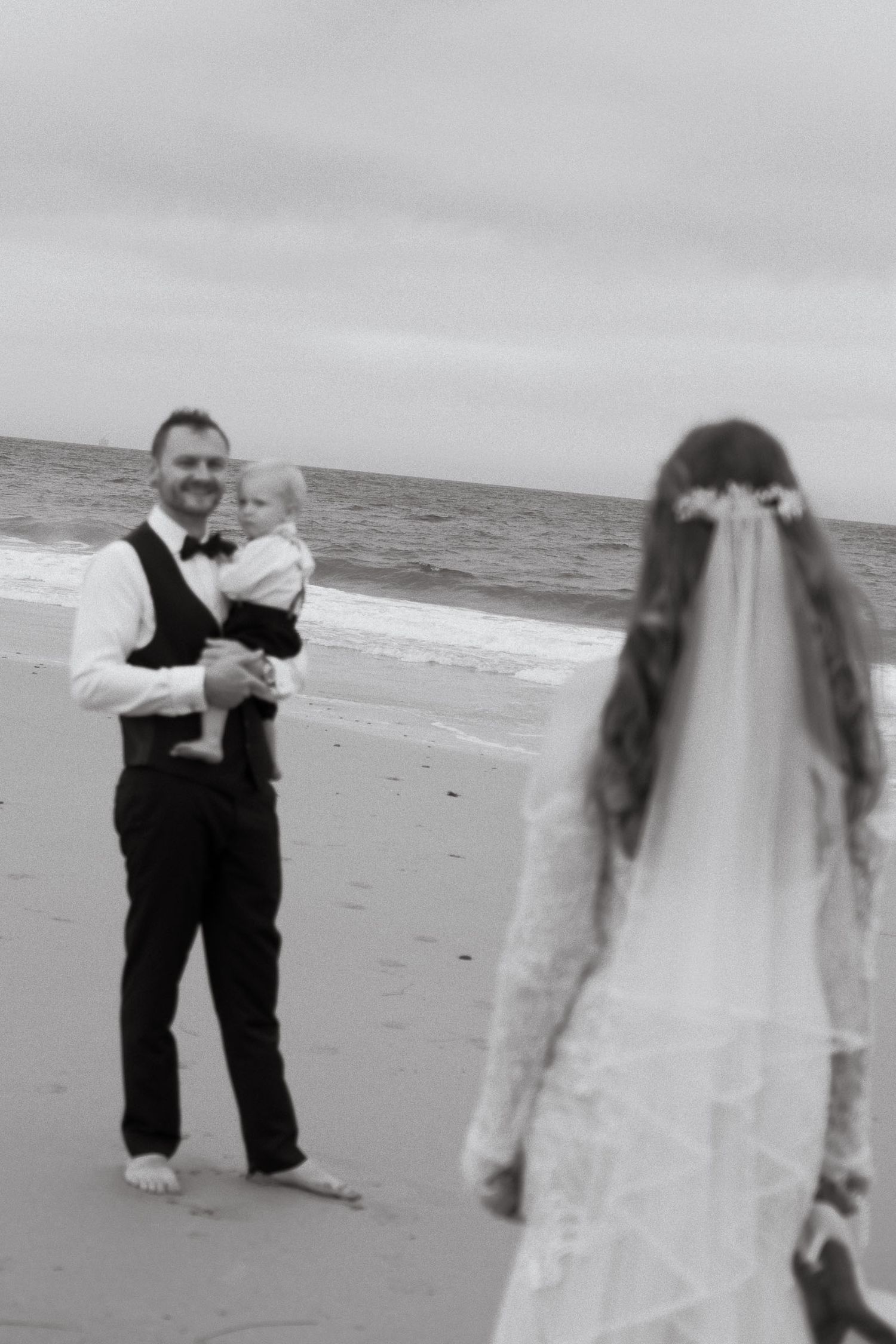 A black and white beach wedding photo shows a couple sharing a moment by the ocean.