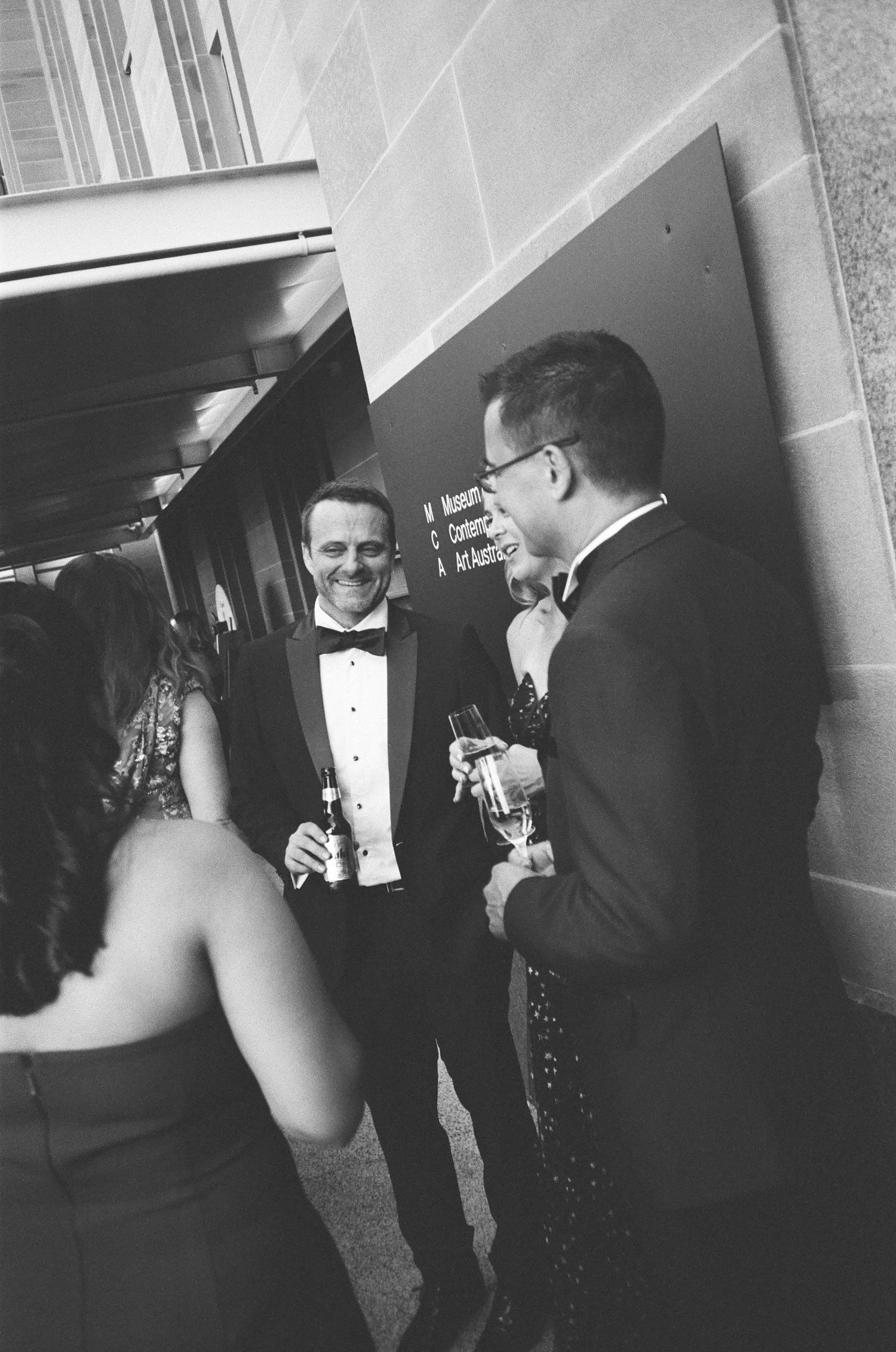 Black and white photo of guests in formal attire mingling at an elegant cocktail reception.