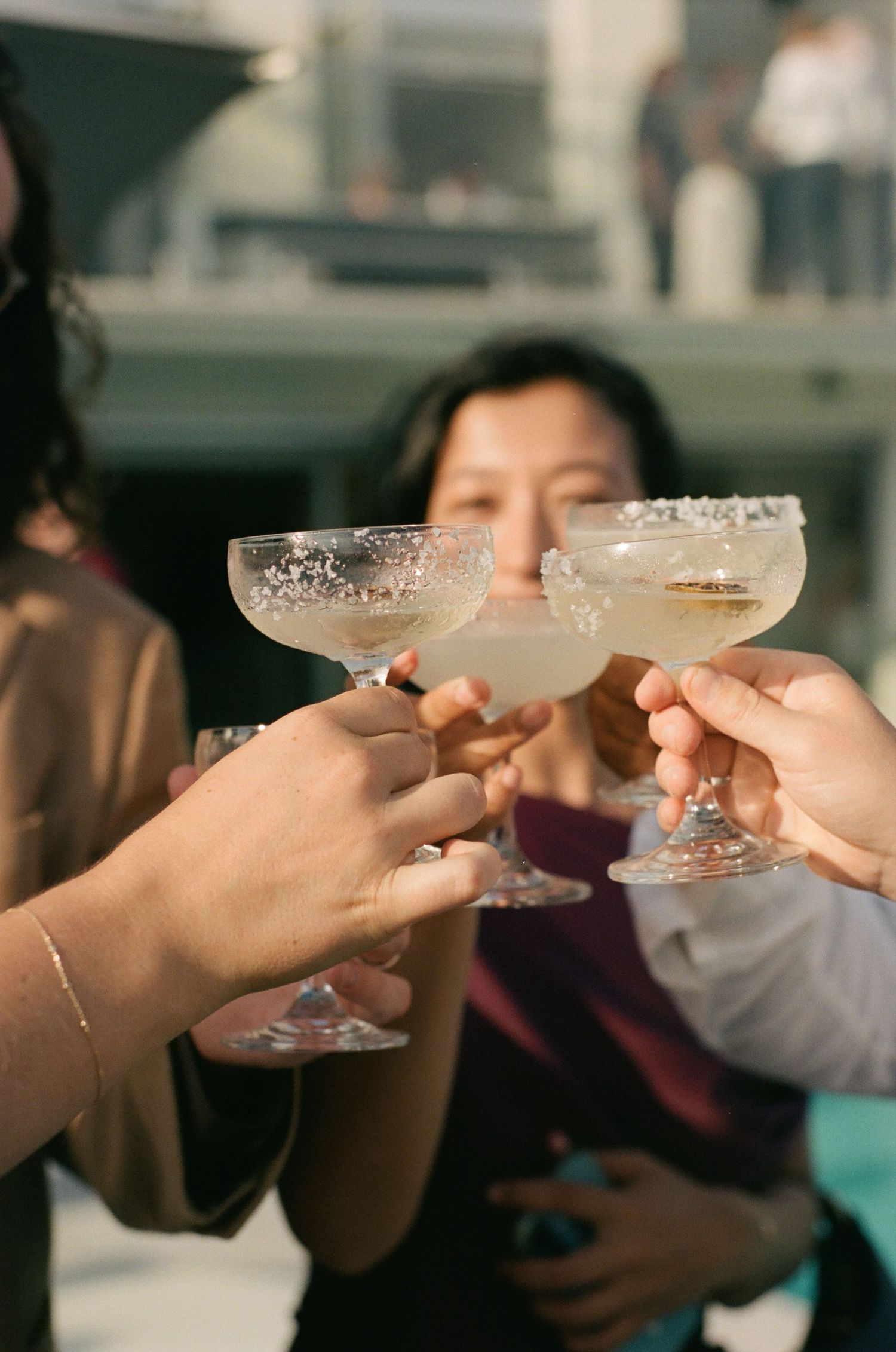 Multiple hands raise champagne glasses with sugar-rimmed edges in a celebratory toast at a social gathering.