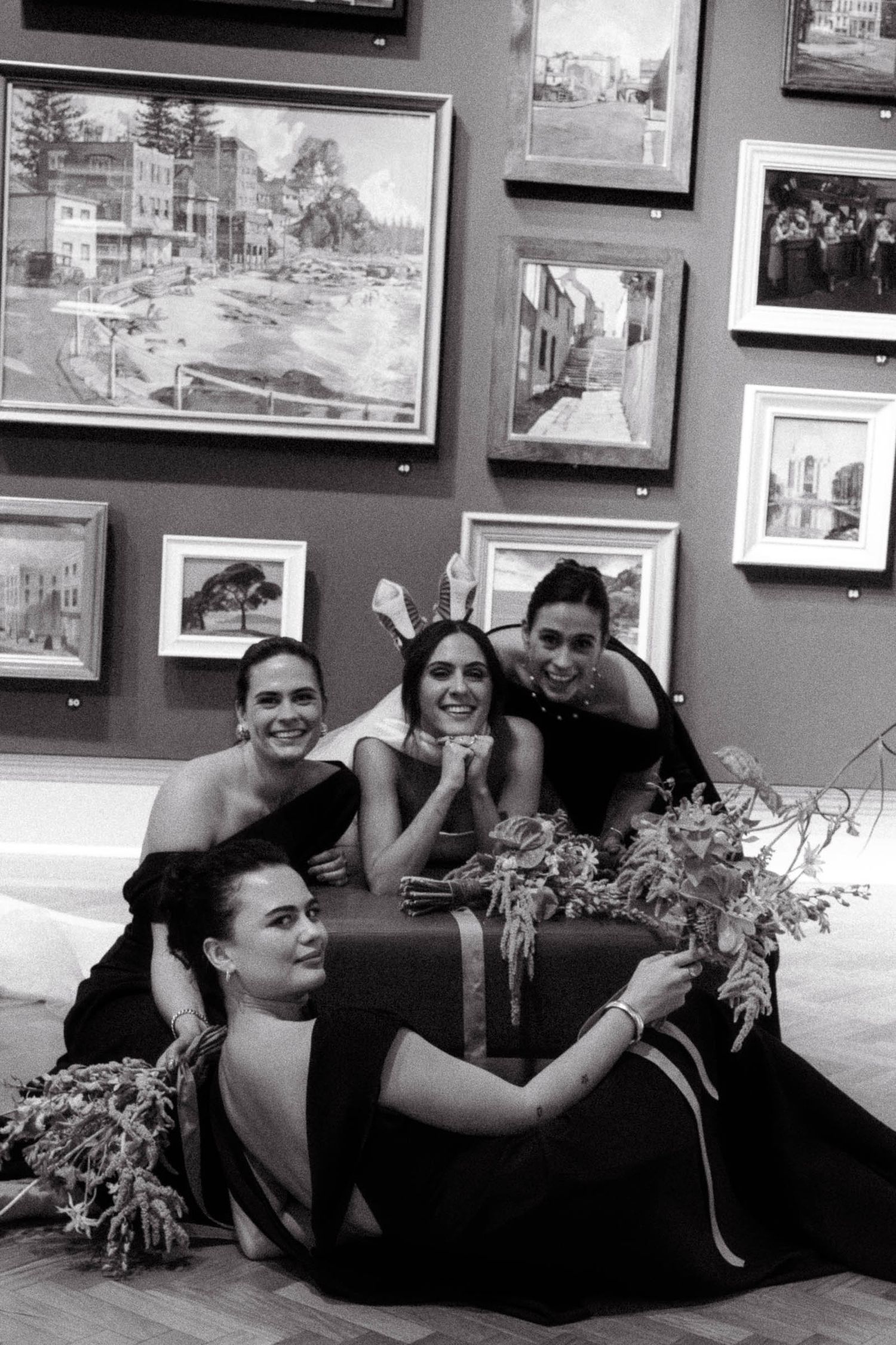 A black and white art gallery wall displays framed photographs above a dark couch with decorative plants.