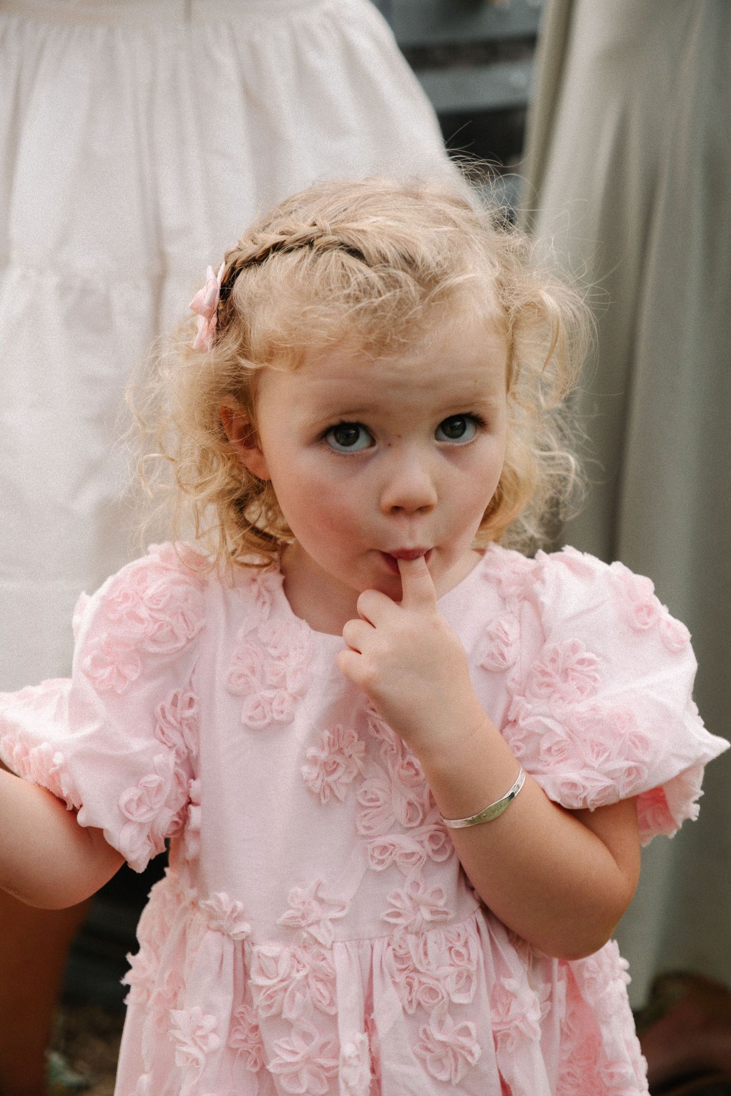 A small child in a pink ruffled dress makes adorable expressions in a series of connected photos.