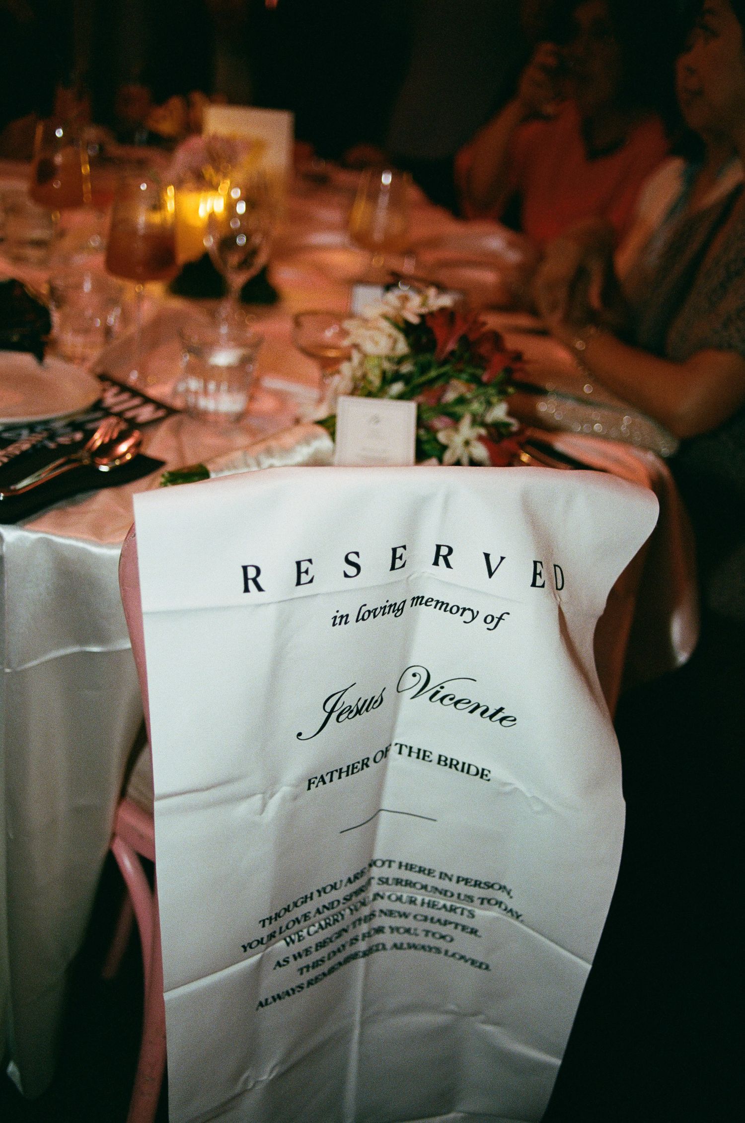Reserved chair banner honoring the late father of the bride, with a floral arrangement at a candlelit wedding reception table.
