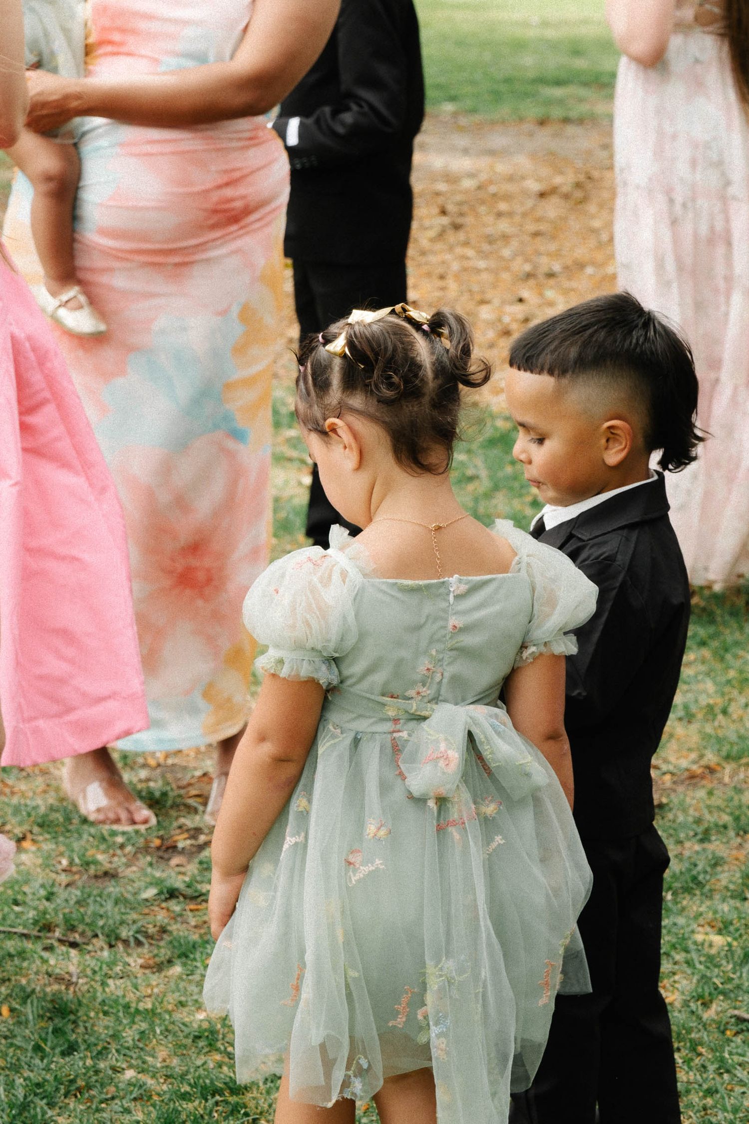 Children in formal attire gather outdoors, with some wearing pink dresses and others in mint green tulle dresses.