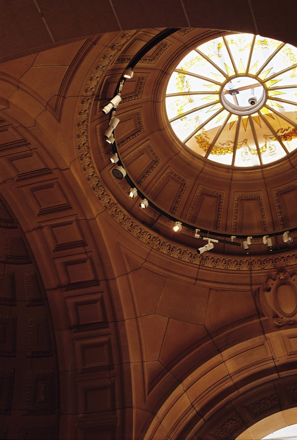 Ornate architectural detail of a domed ceiling with sunburst pattern and decorative moldings in warm lighting.